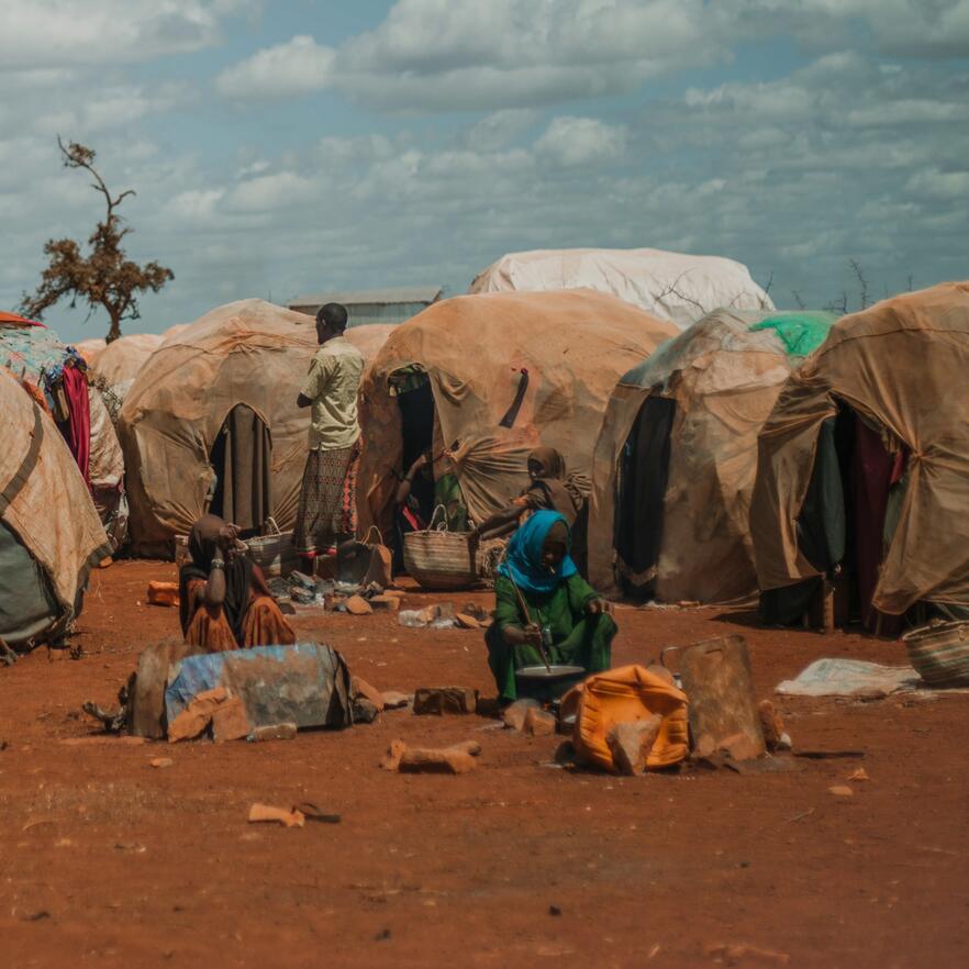 A woman sits on dusty ground by tents in a camp in Somalia for people displaced by drought.