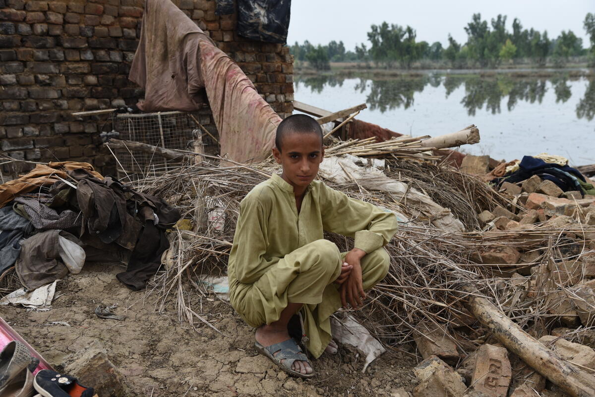 A young Pakistani boy sitting in front of his home ruined by floods