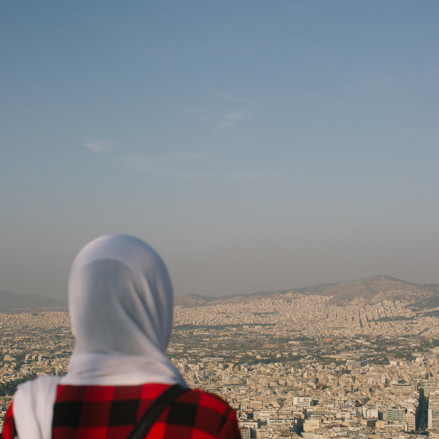 Fariba stands with her back to the camera and overlooks the city of Athens, Greece.