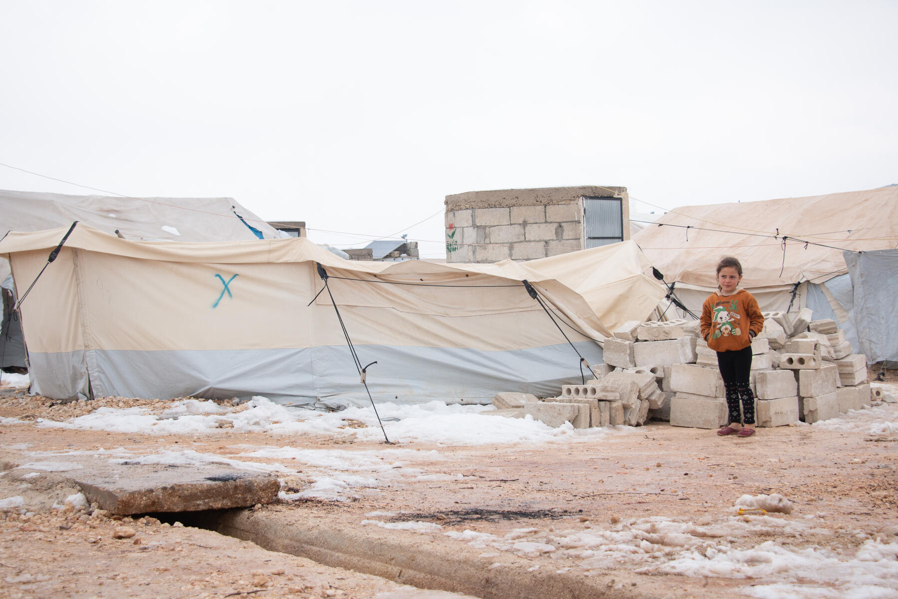Young girl stands in front of her home in displacement camp, Syria.