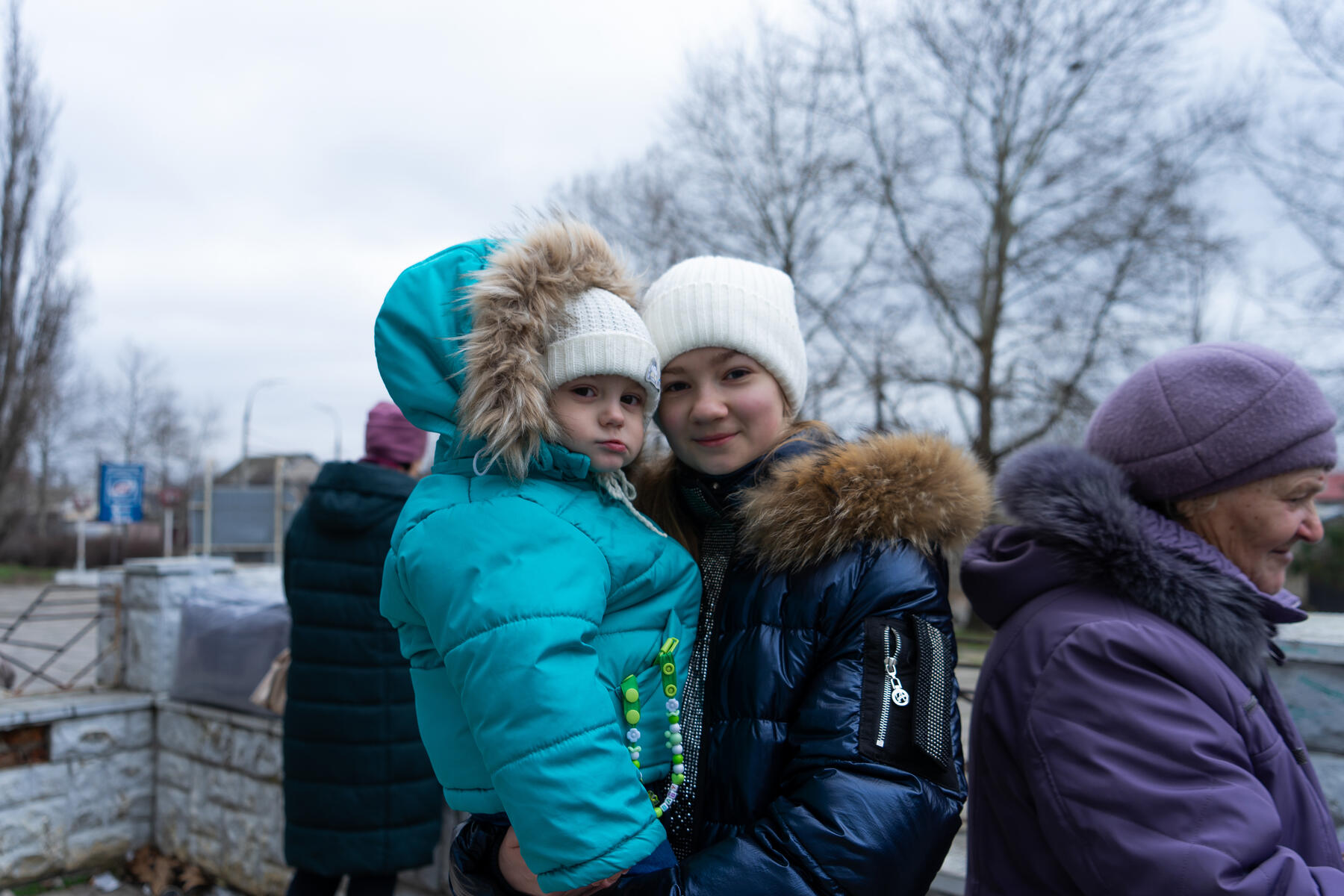 Young girl stands, carrying her baby sister, both facing the camera.