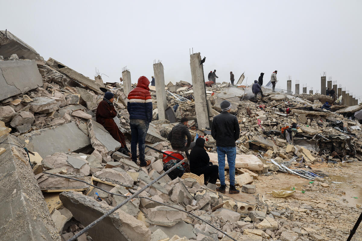 A group of survivors standing in rubble following the February 2023 earthquake in Syria.