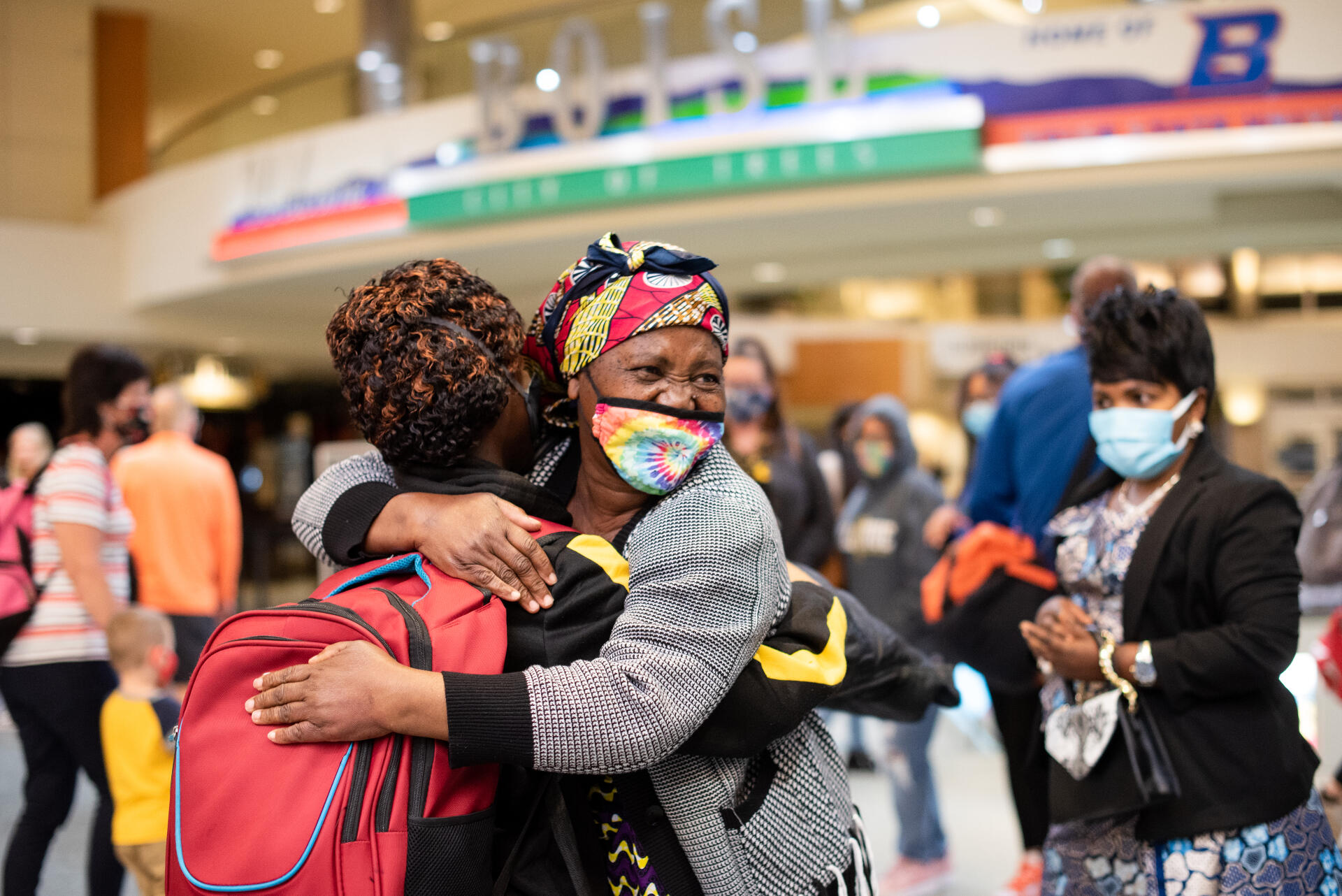 A refugee family is reunited at an American airport. The family hug each other in a warm embrace and smile.