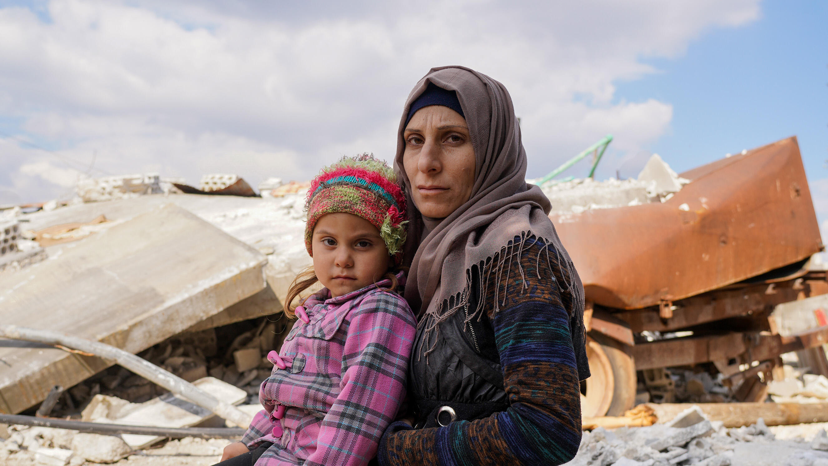 En mamma och hennes barn sitter på ruiner efter jordbävningen i Turkiet och Syrien. 