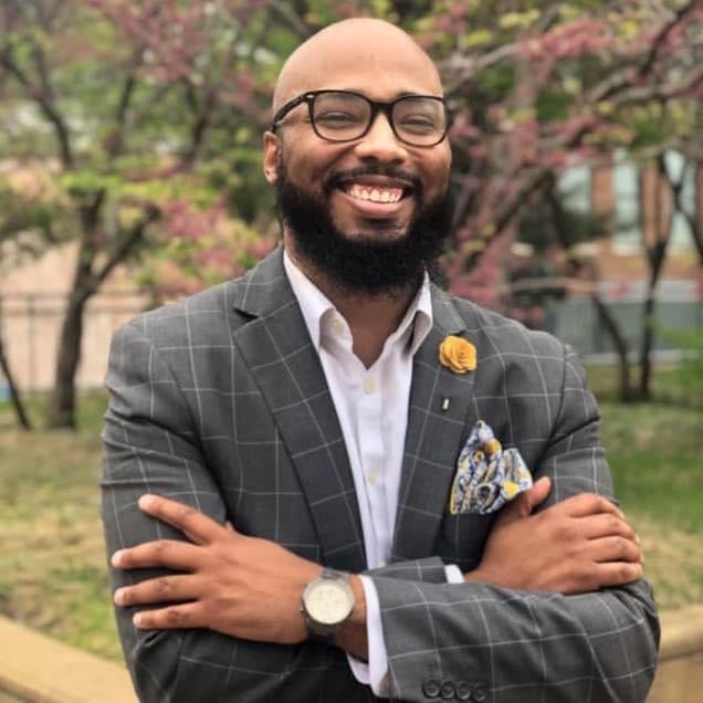 Image of Darryl Young Jr., Executive Director of the IRC in Louisville, wearing a gray suit, glasses, and a watch; he is smiling with his arms crossed.