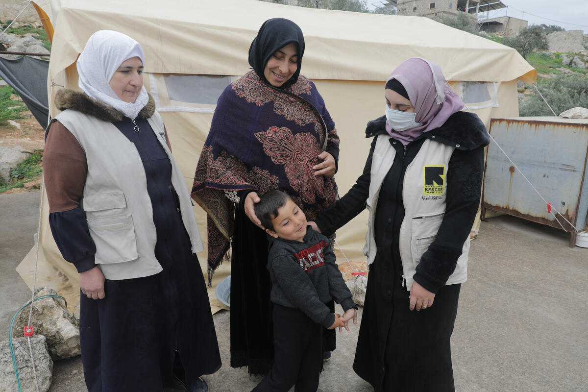 An IRC worker talking to Syran women and a young child