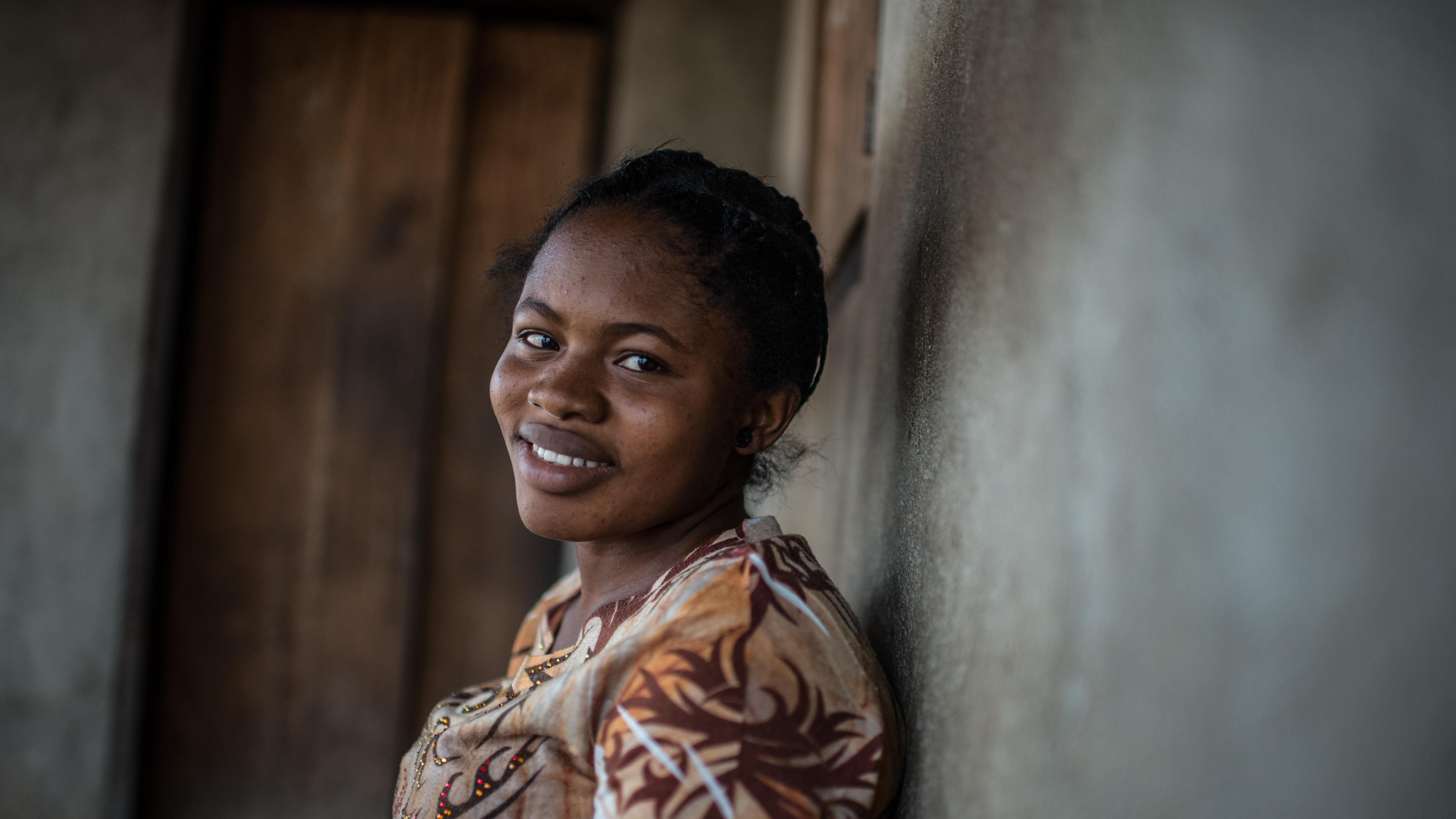 A woman leans against a wall and poses for a photo.