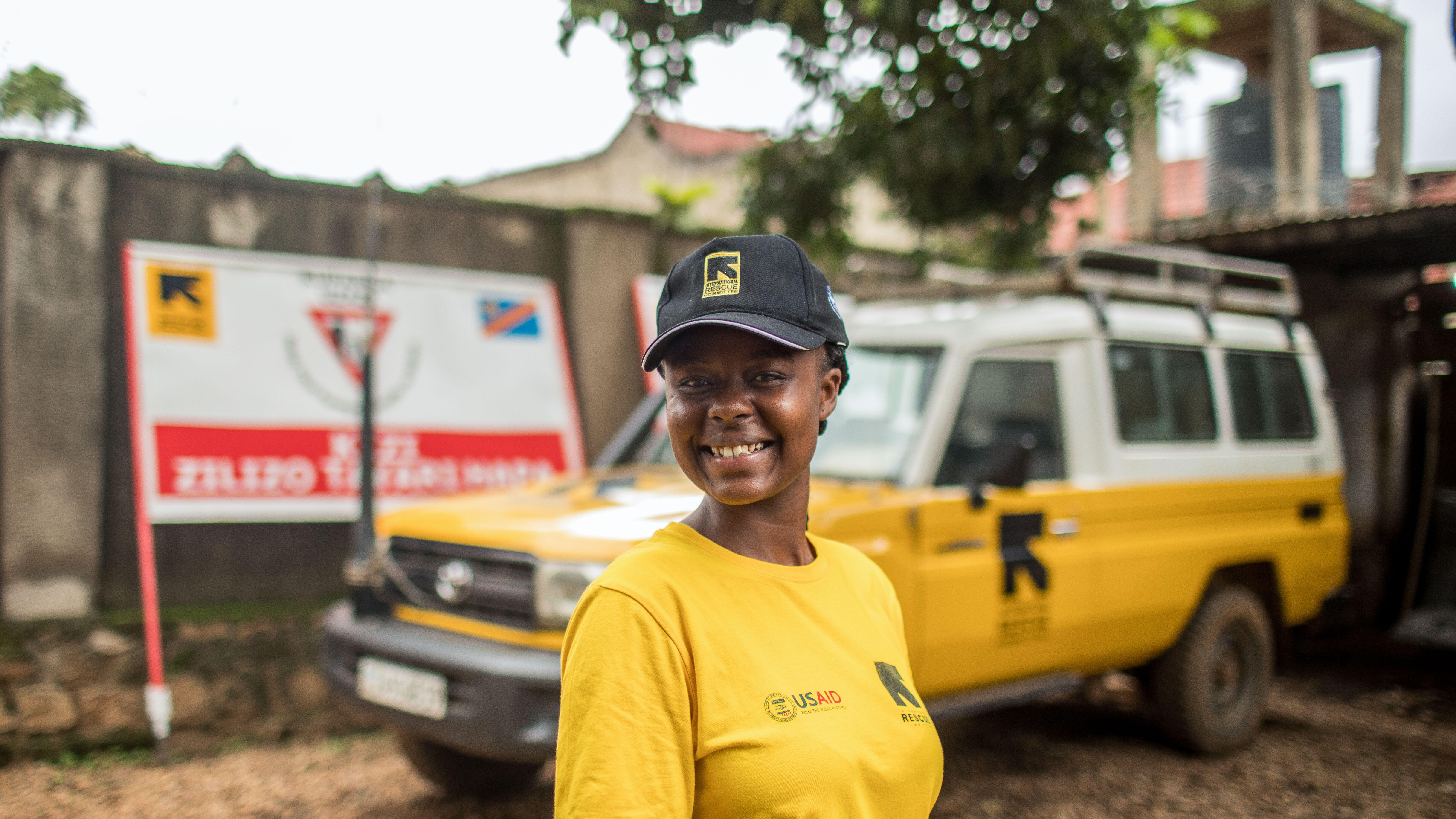 A woman wearing an IRC shirts smiles in front of an IRC branded truck.
