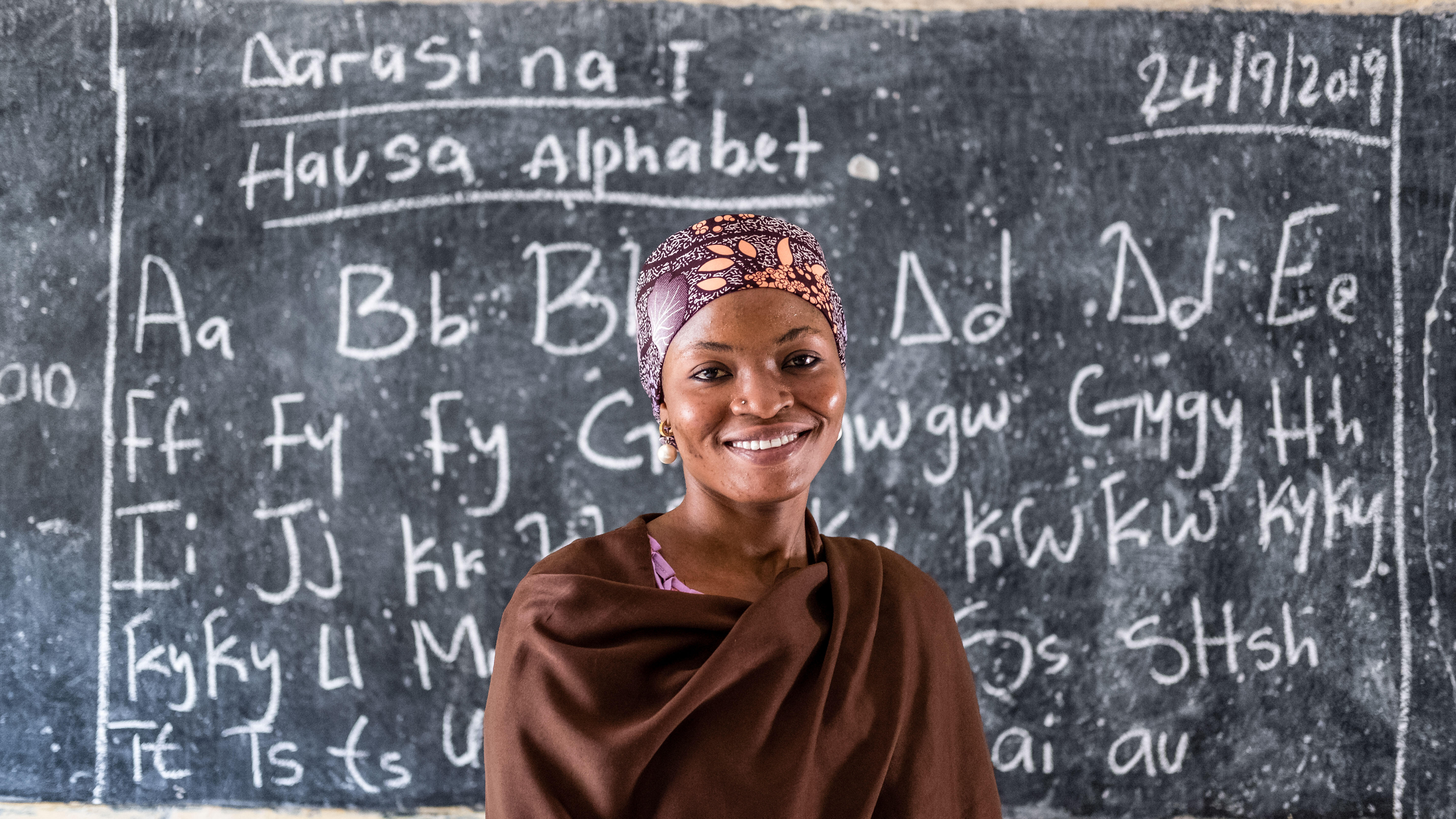 A girl stands in front of a school chalkboard.