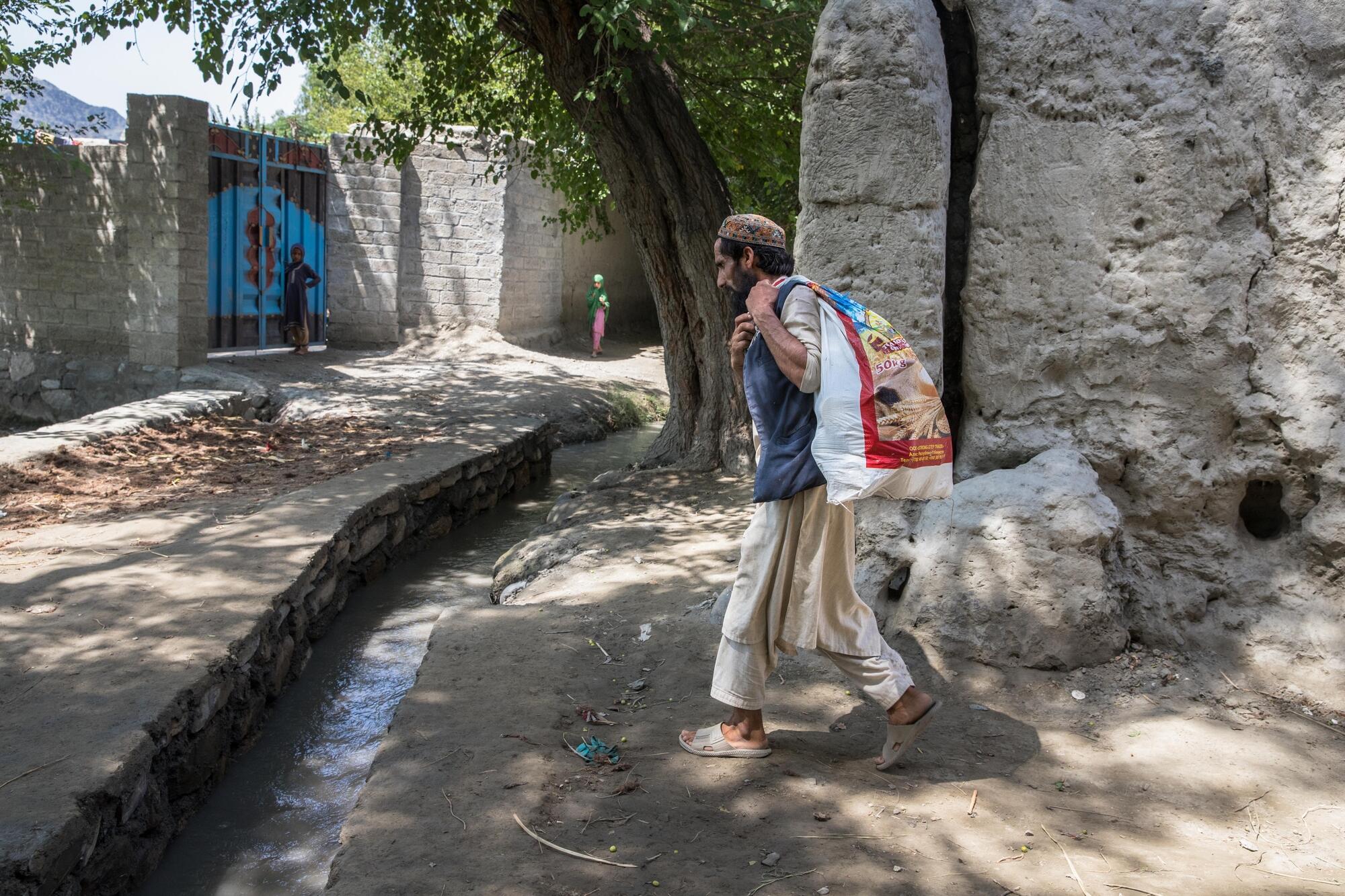 A man walks with a sack over his back, filled with pickles to sell at the bazar.