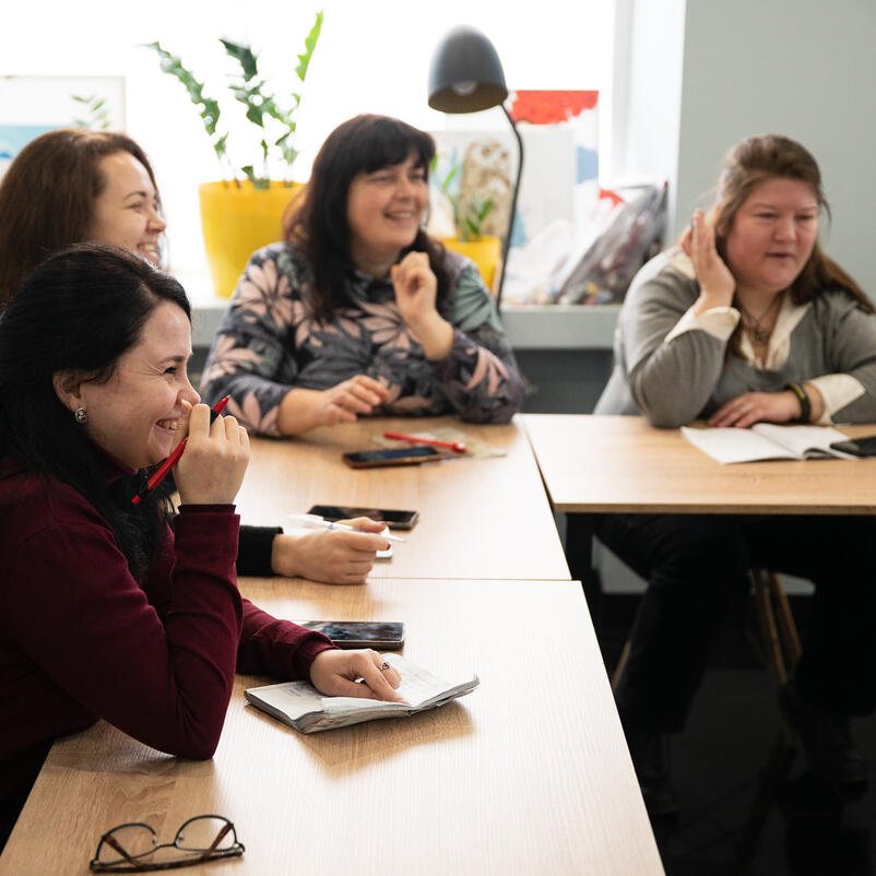 Women sit around the table talking and laughing in a Dnipro safe space funded by the EU