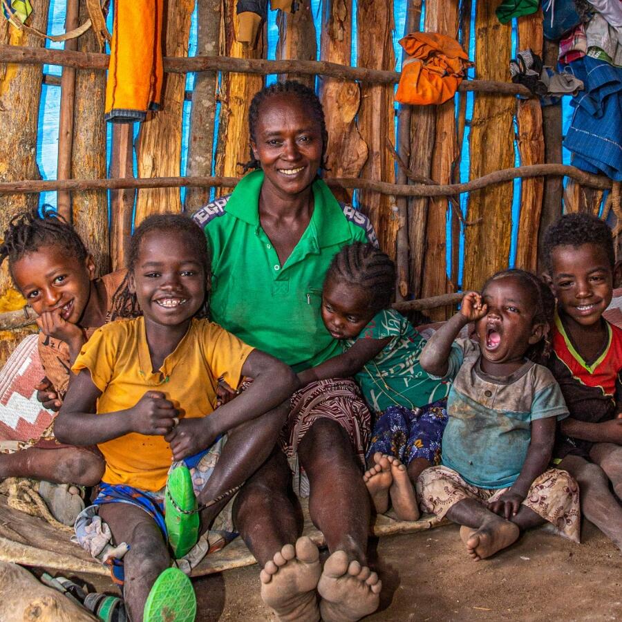 Mengesha, in a bright green shirt, sits smiling with five of her children, in an internally displaced persons camp in Ethiopia.