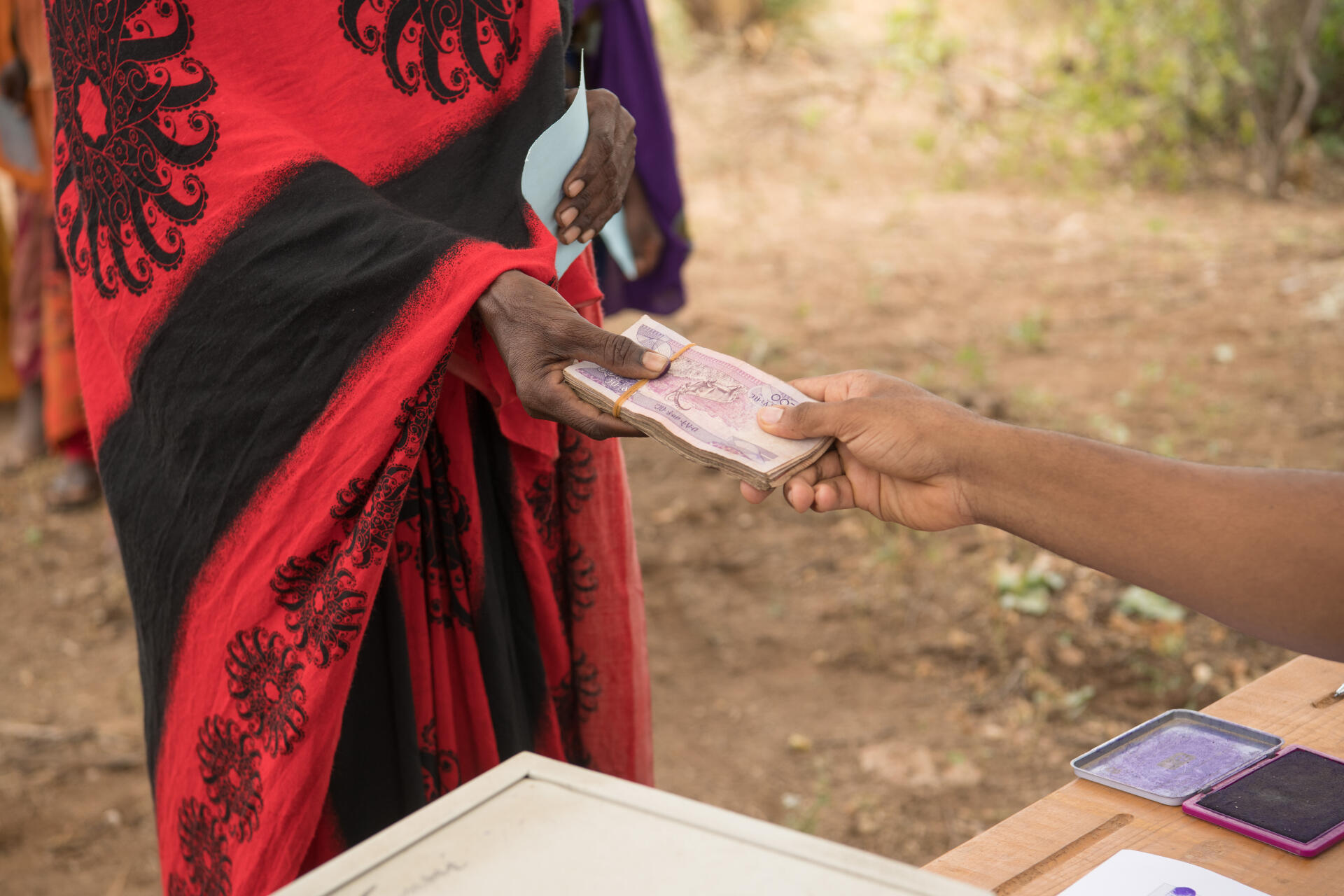 Two people exchange a stack of Ethiopian currency. The bills are pink in color.