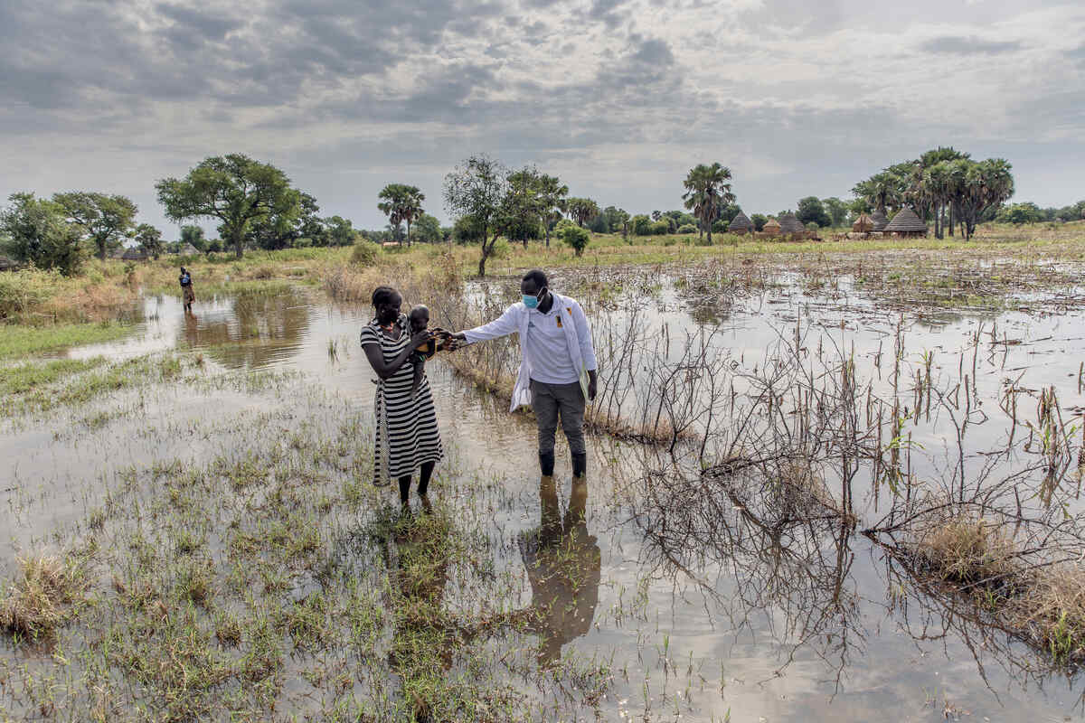 Abuk Deng holds her four year old daughter in her arms as they walk through a flooded field with an IRC malnutrition officer.