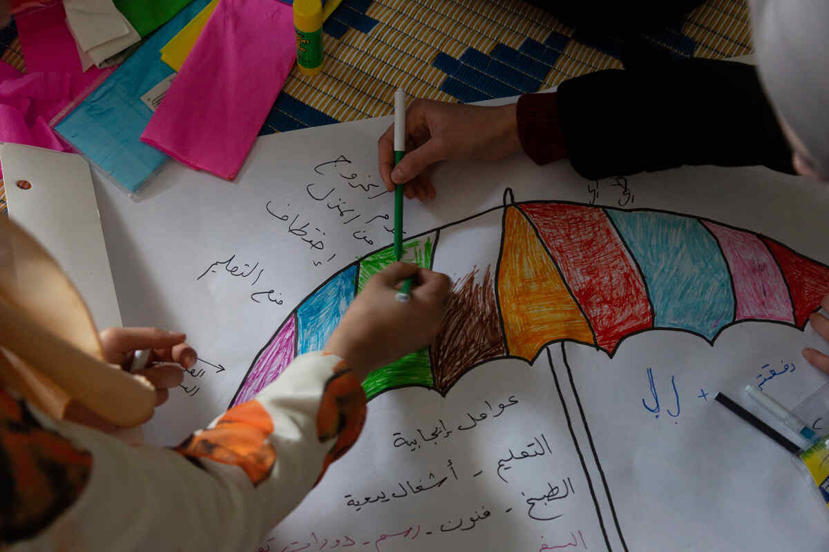 Syrian refugee girls color and write on a carton on the floor in the safe space where they take part in different kind of activities with the IRC WPE team.