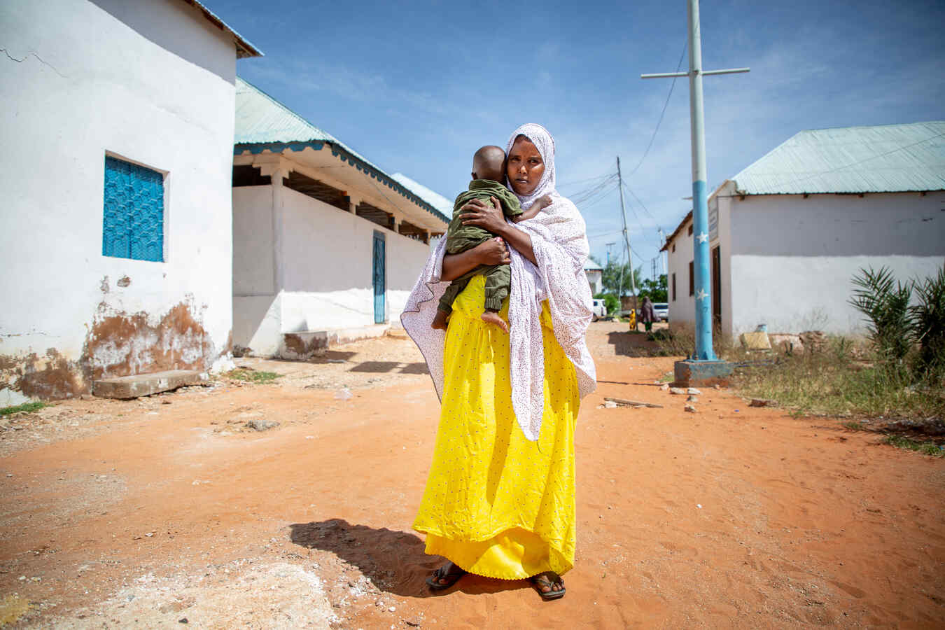 Fartun stands in the street, holding her baby son.