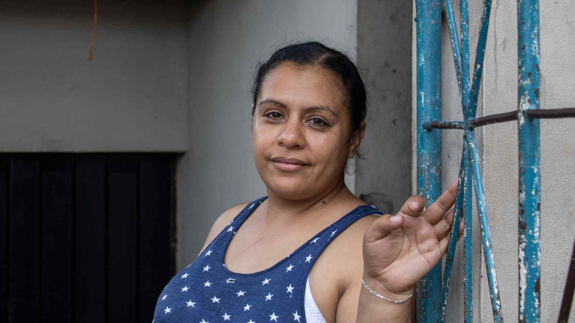 A Honduran woman poses for a portrait photo next to a blue gate.