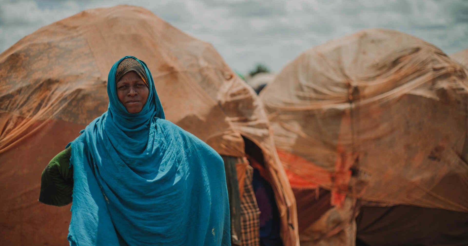 A woman poses for a photo outside of a small structure covered in blankets in Torotorow IDP Camp, Somalia.