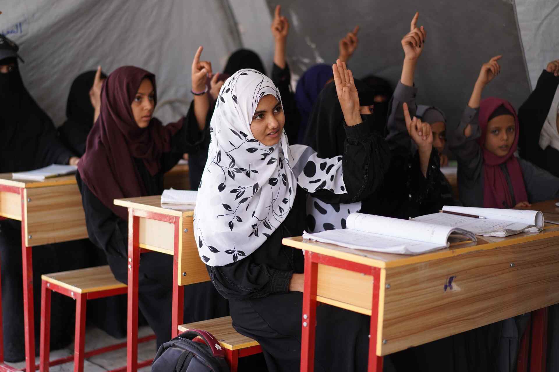 Photo of a classroom of girls in Yemen, raising their hands during a lecture. 