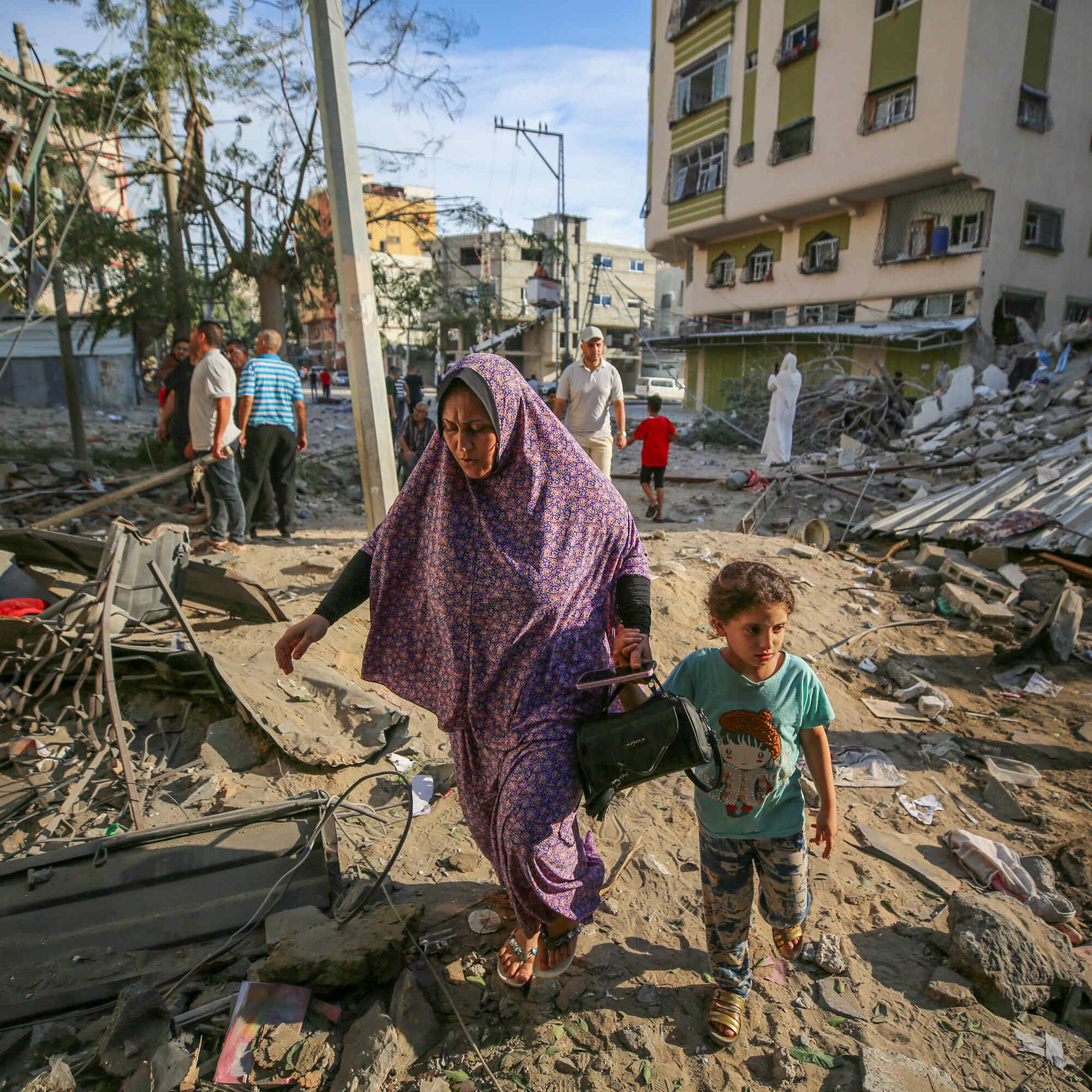 A woman and child walk through rubble, while people nearby assess the destruction cause by Israeli air strikes in Gaza City on October 7, 2023.