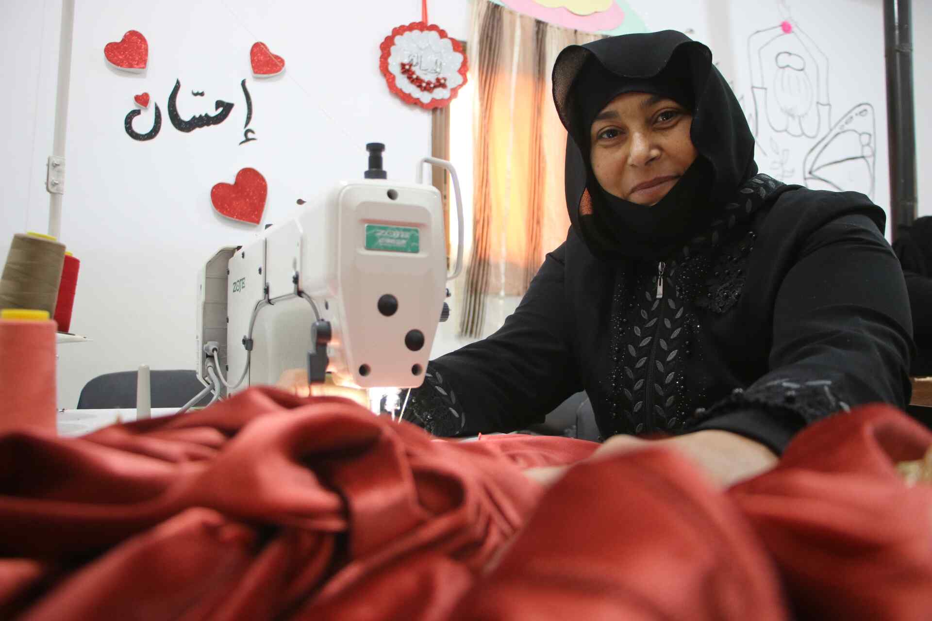 Mustafa sews a red piece of clothing.