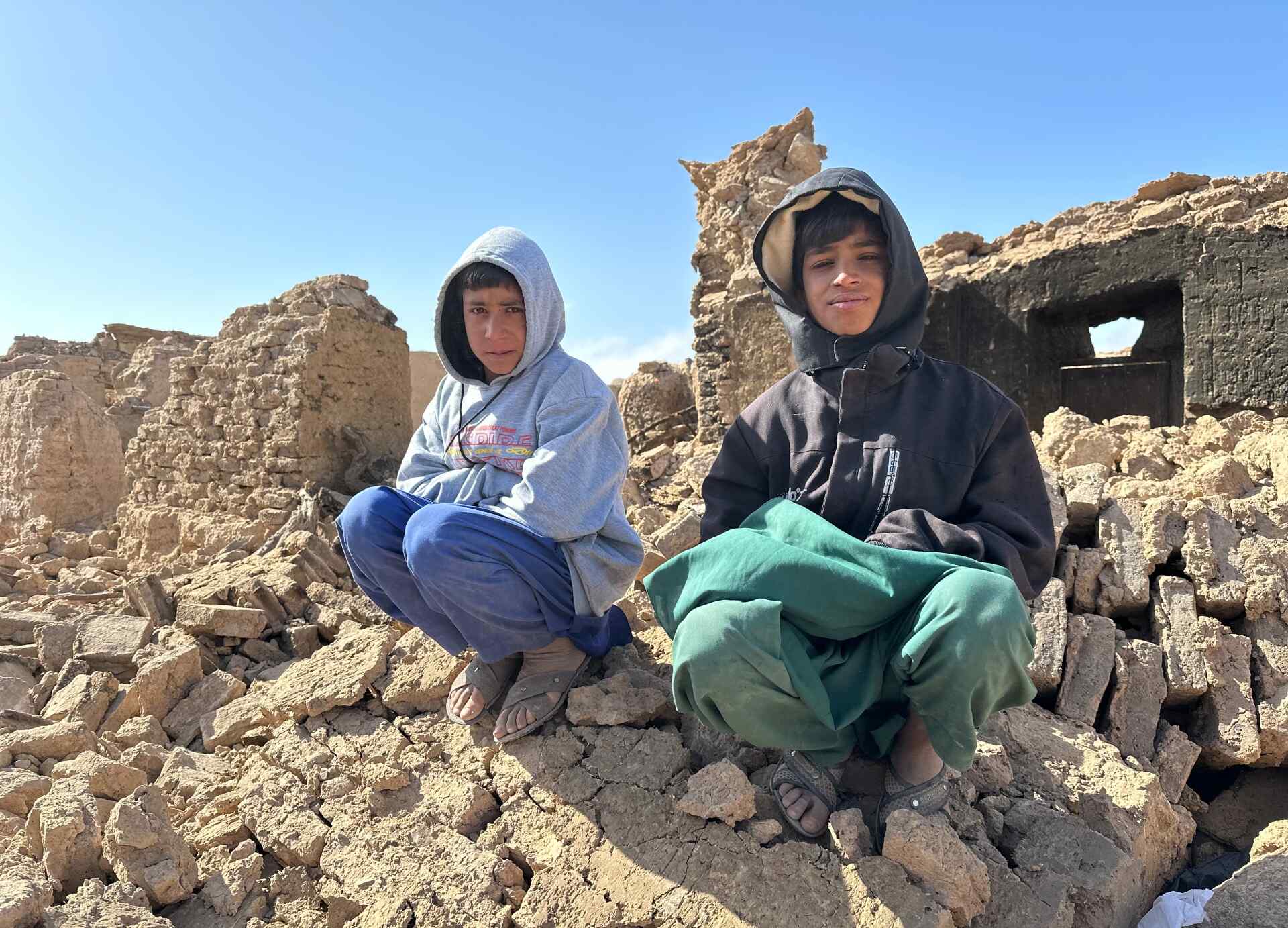 Two Afghan boys sit atop a pile of rubble from a building destroyed by an earthquake.