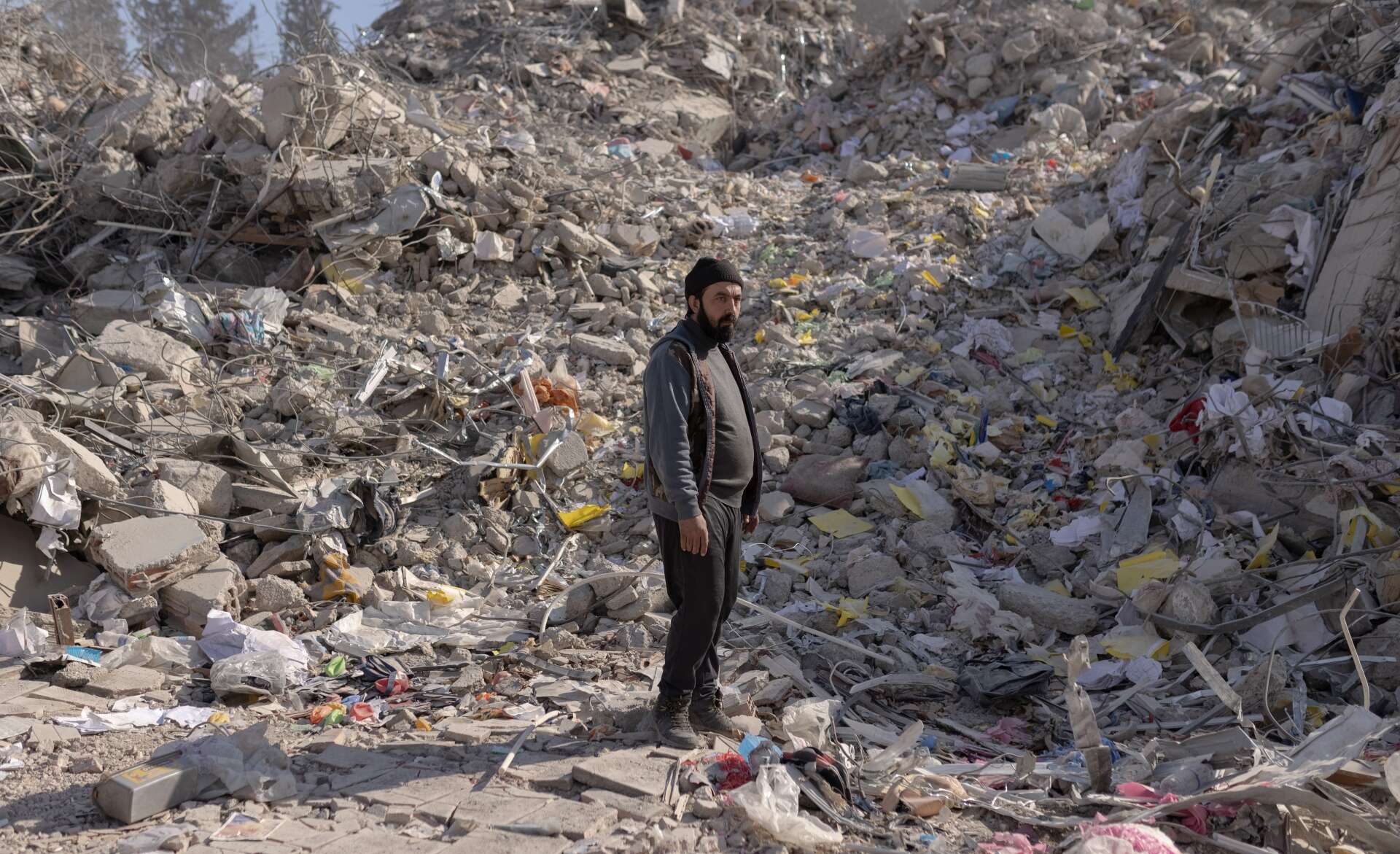 A man stands in the midst of the rubble of a building destroyed in the Syria-Turkey earthquake.
