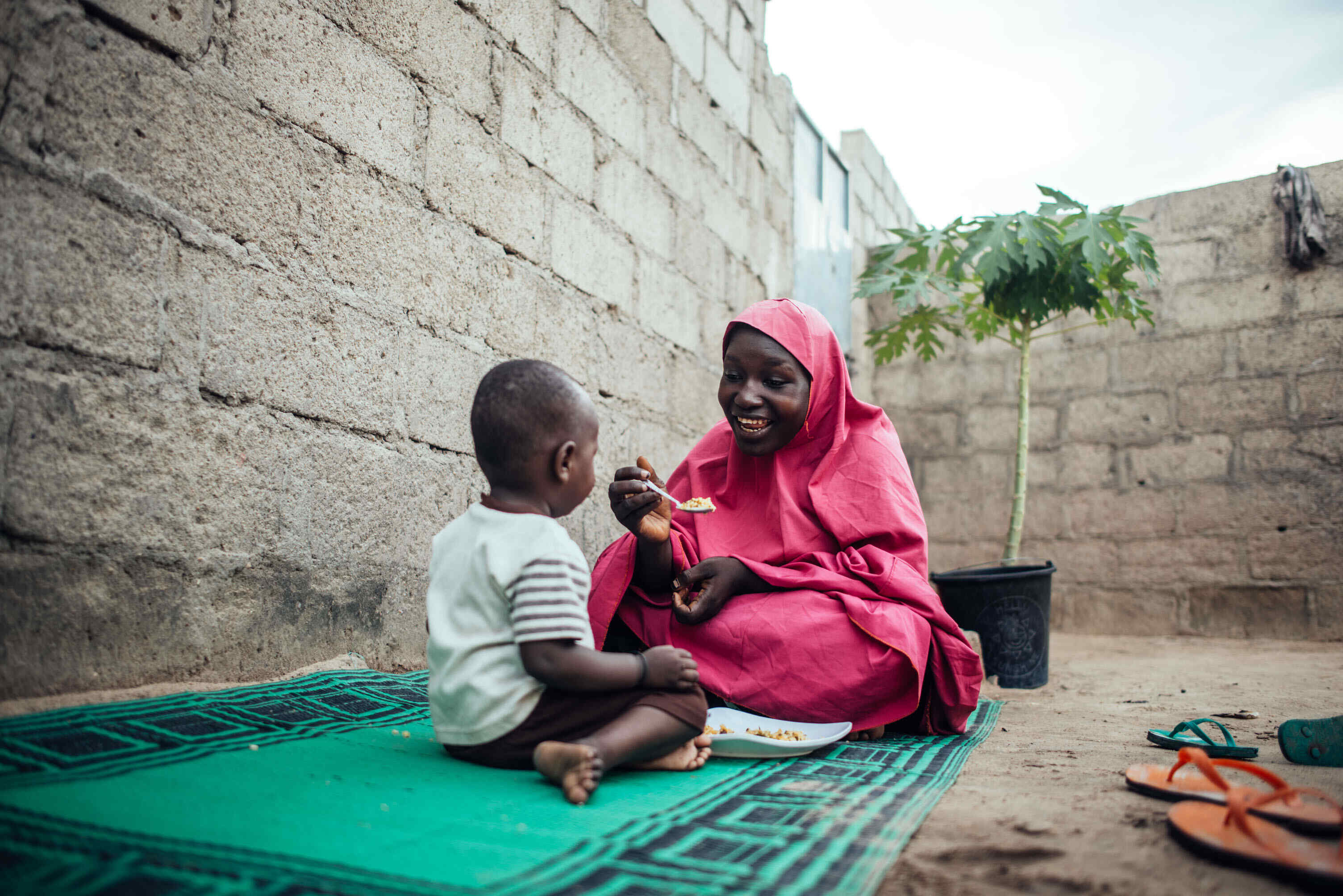 나이지리아의 한 엄마가 자녀에게 웃으며 밥을 먹이고 있습니다.