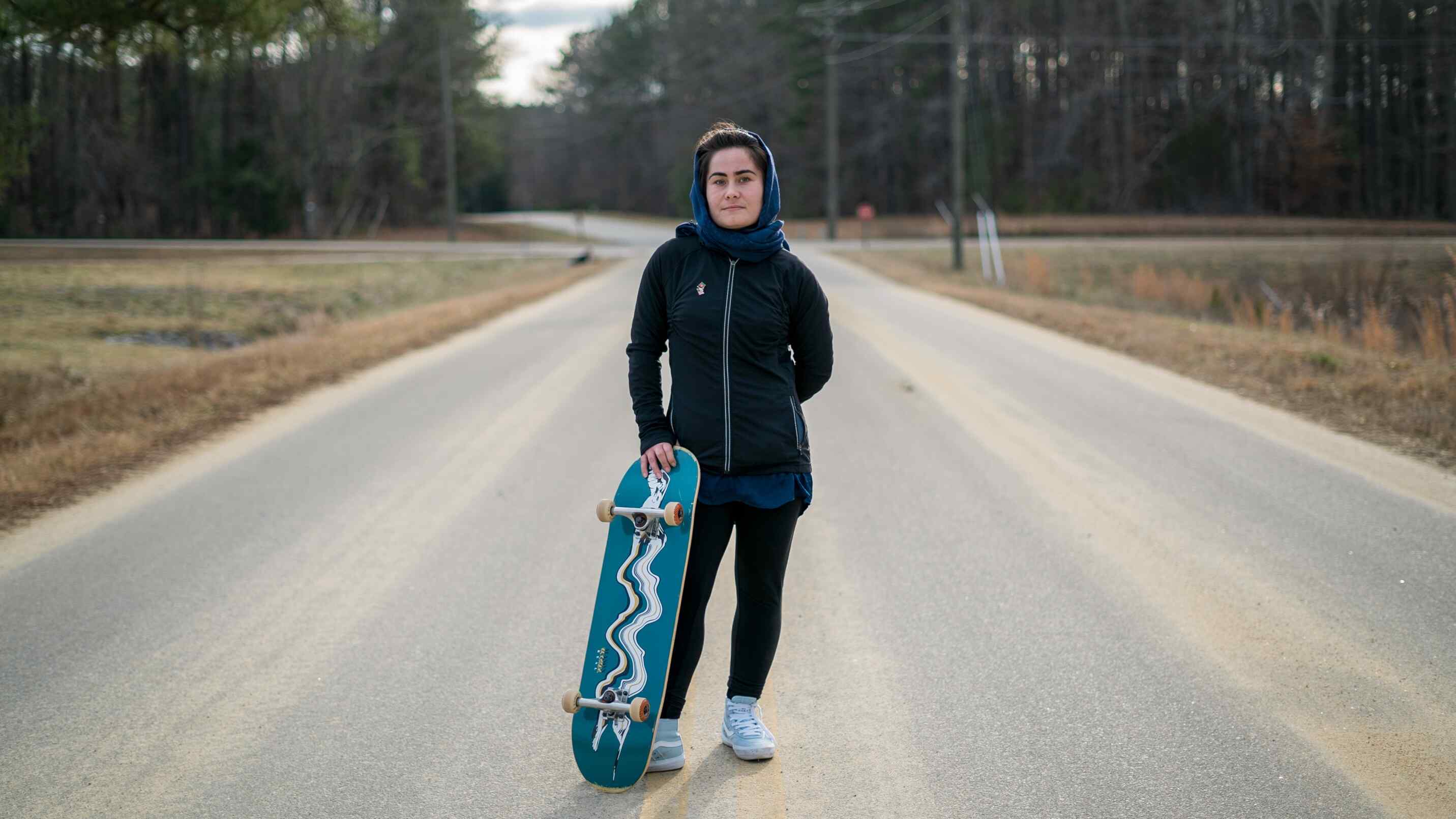 An Afghan refugee poses for a photo while holding her skateboard.