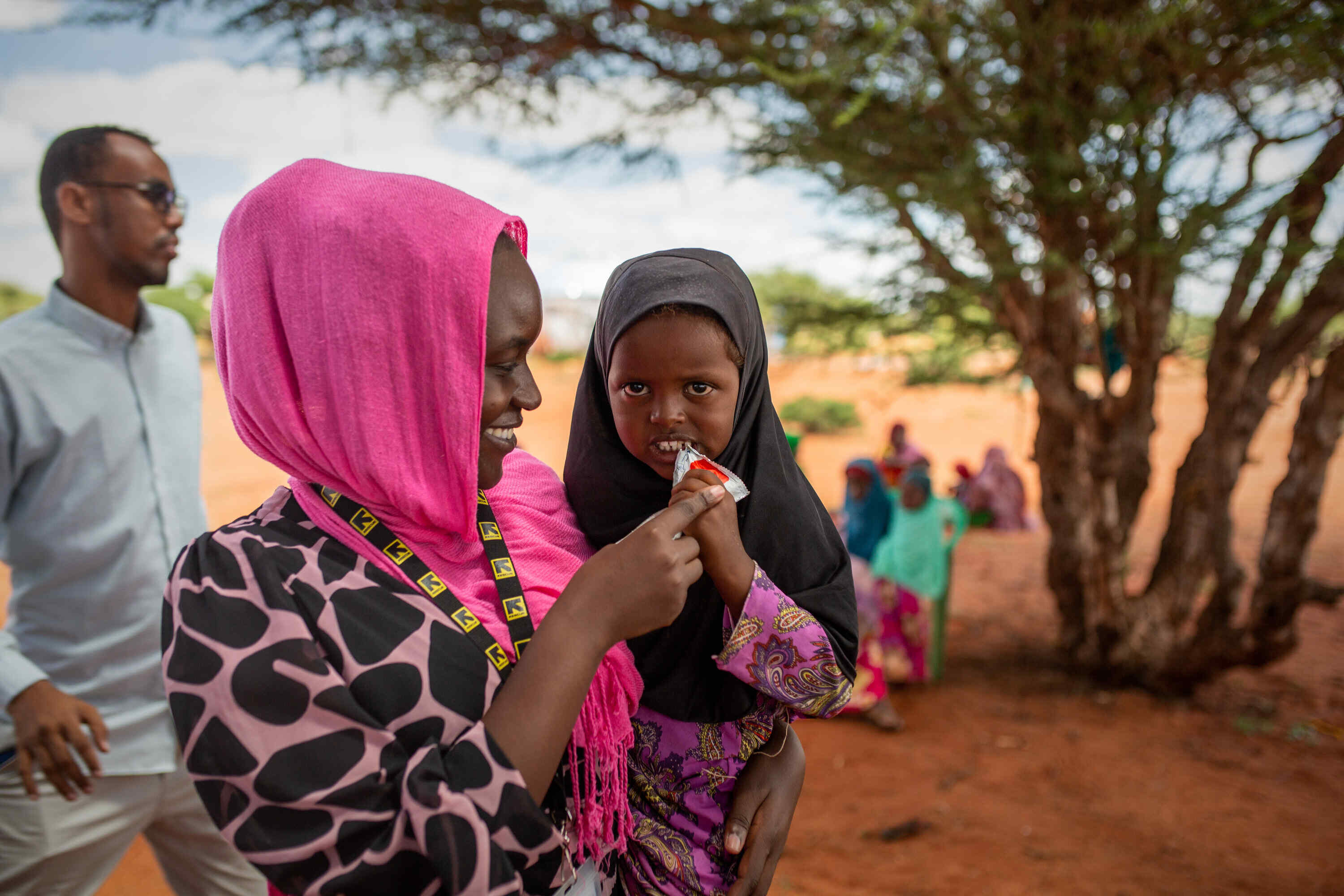 IRC staff with young girl eating PlumpyNut in Olol Village, Somalia