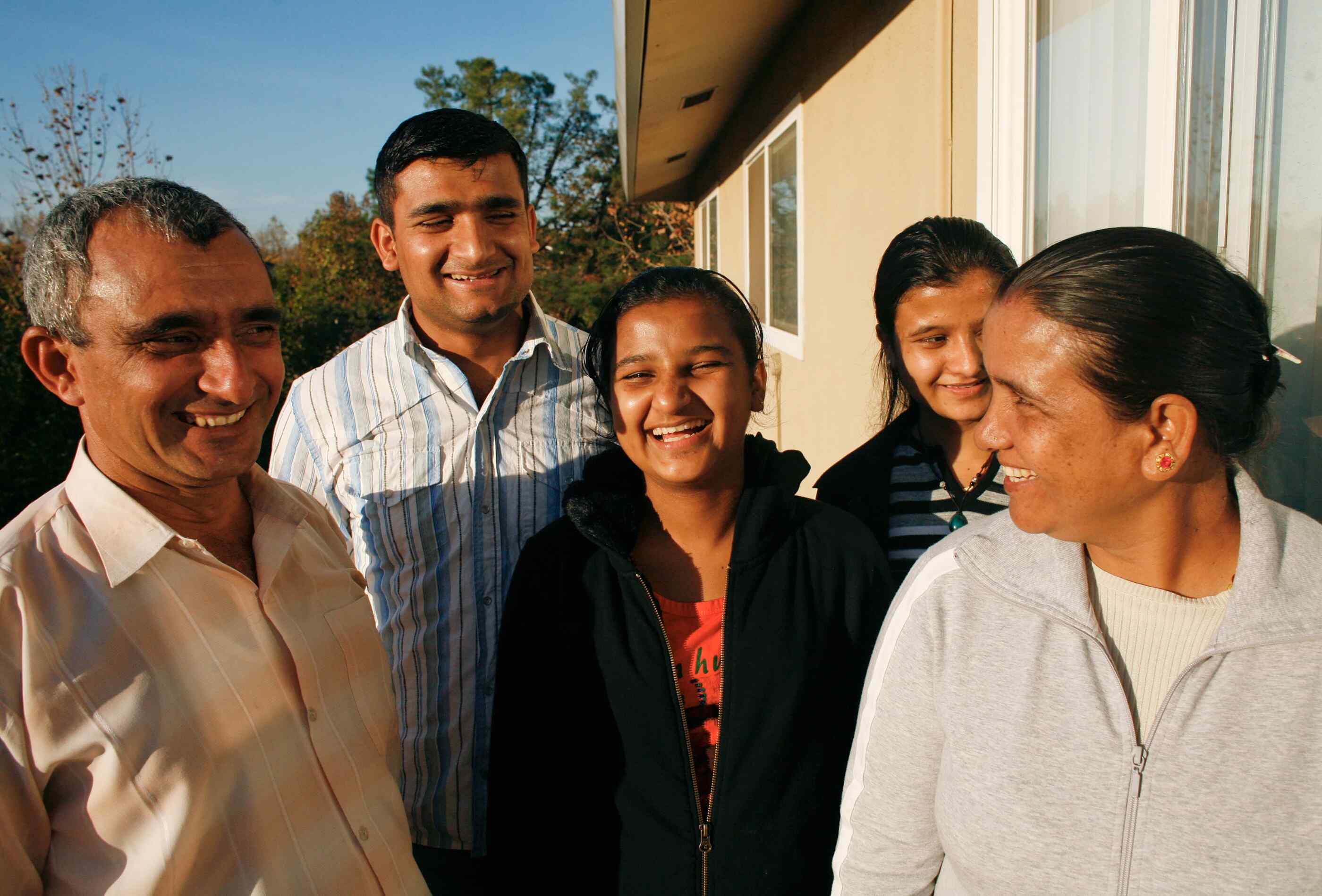 Family of five stands outside its Sacramento home, laughing together while their picture is taken.