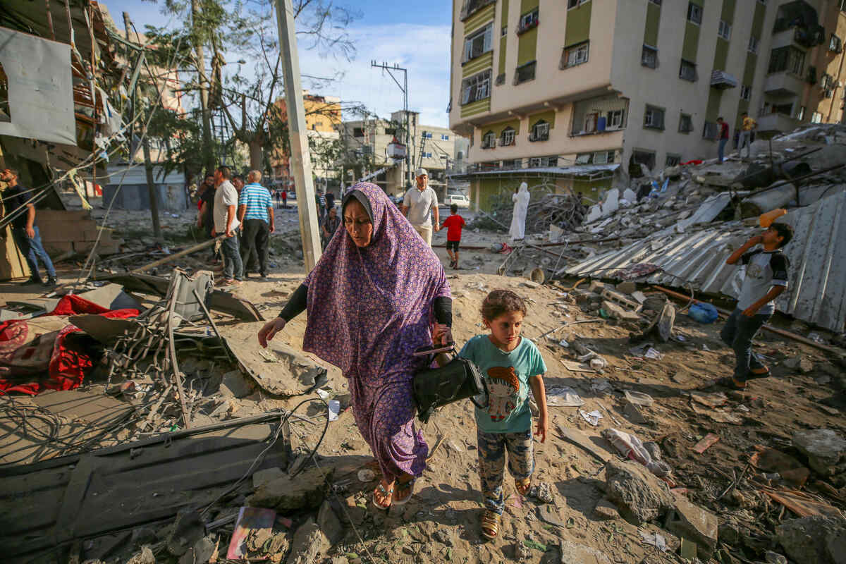 A Gazan mother makes her way through the rubble with her small child