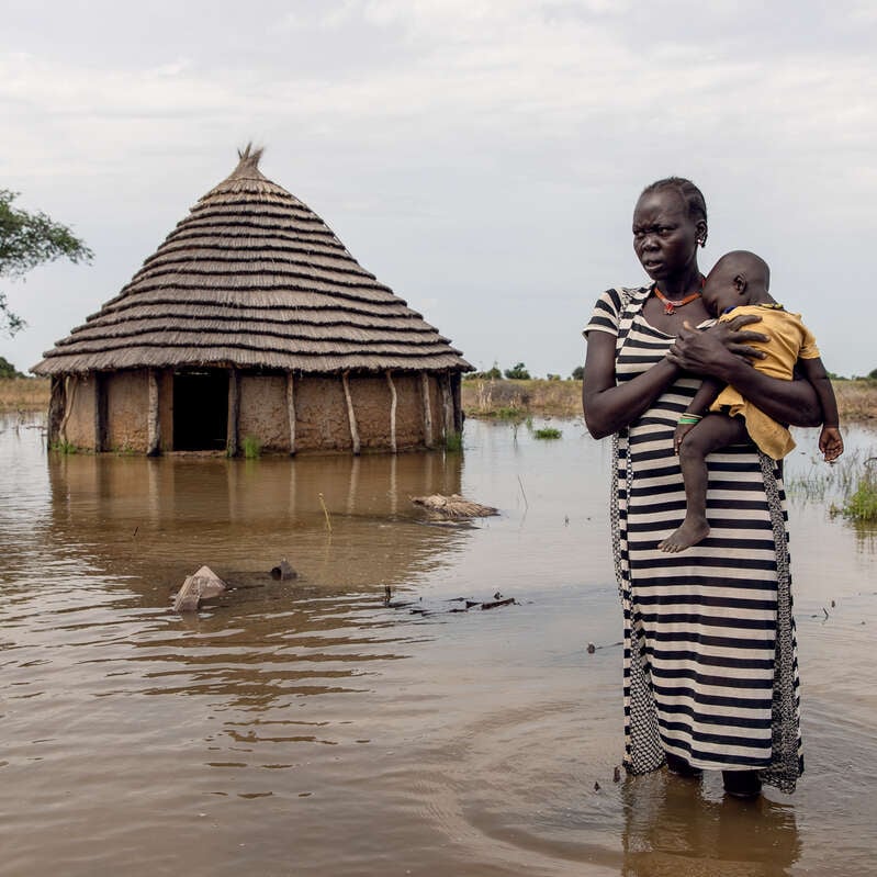 Abuk, 30, holds her daughter, Nyirou, 4, in front of their flooded home in Northern Bahr el Ghazal, South Sudan.
