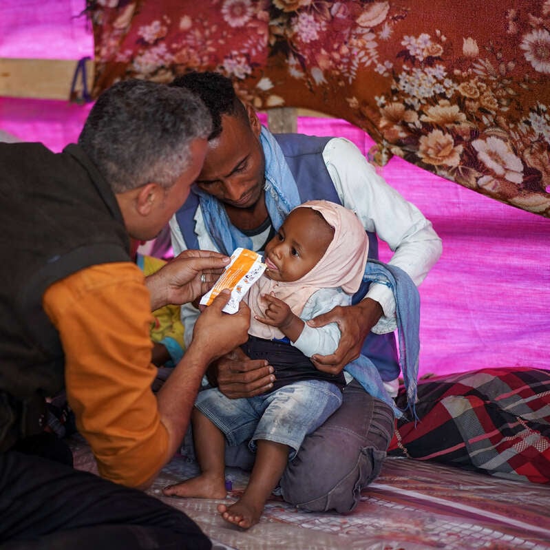 While the child Ahlam, 10 months old, is eating peanut paste which will help her health improve. Dr. Ala’a is an IRC Nutrition Officer in Yemen. He and his team operate mobile medical clinics that reach displaced families in rural areas and camps with urgently-needed medical care, including treatment for children facing moderate or severe acute malnutrition.