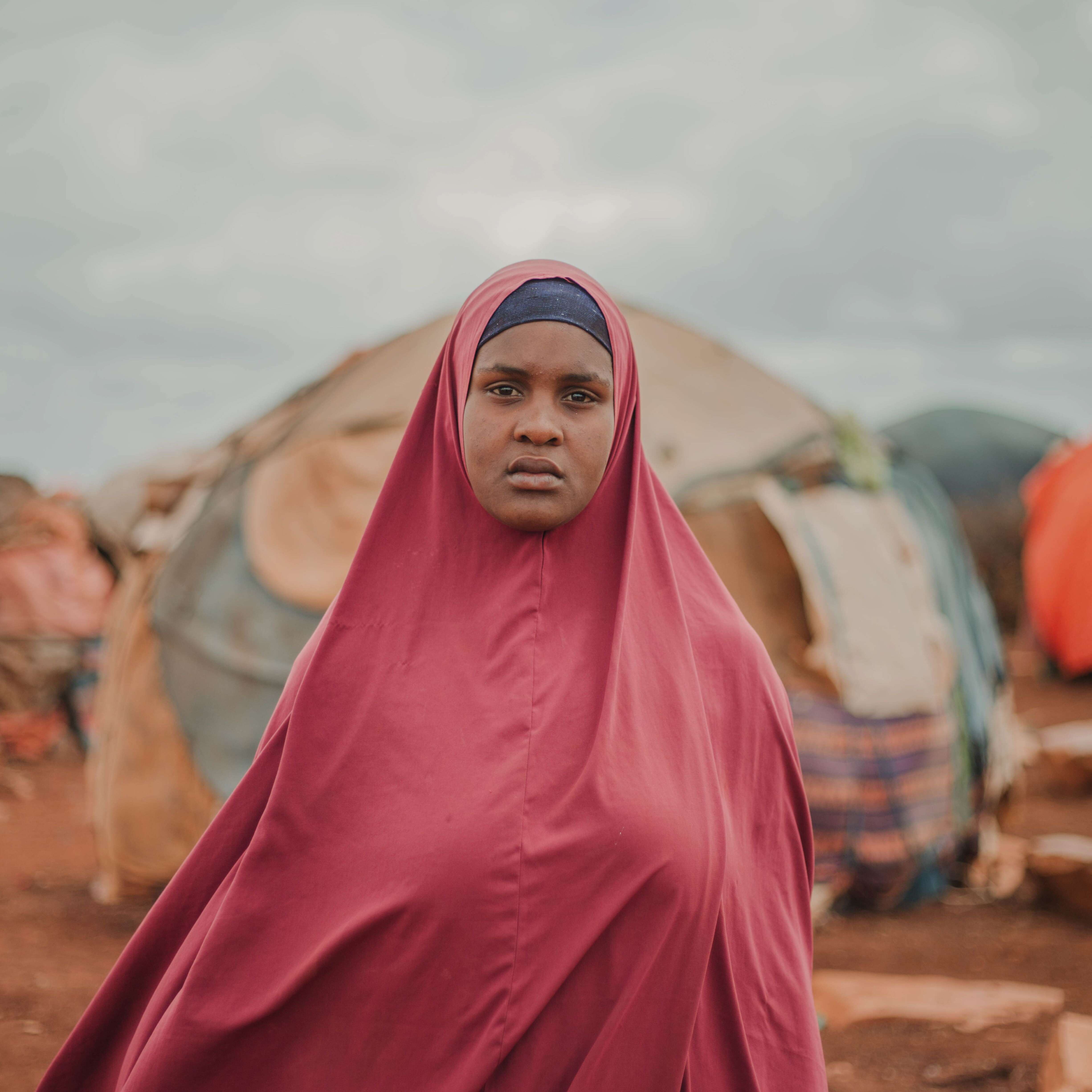 Amina, a refugee living in Somalia, standing in front of an internally displaced persons camp