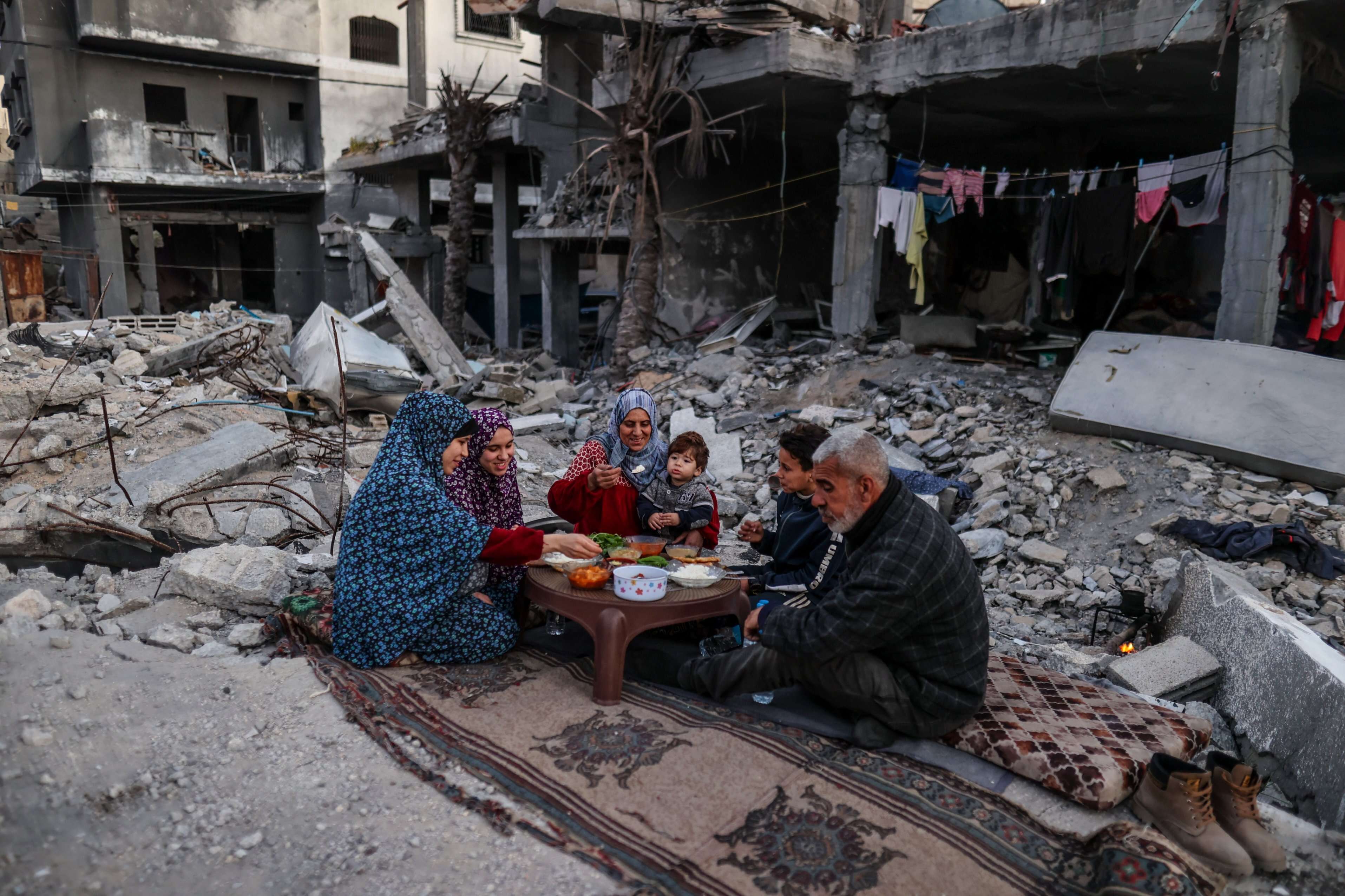 Eine Familie sitzt zusammen inmitten von Trümmern und teilt ihre iftar Mahlzeit während des Ramadan.
