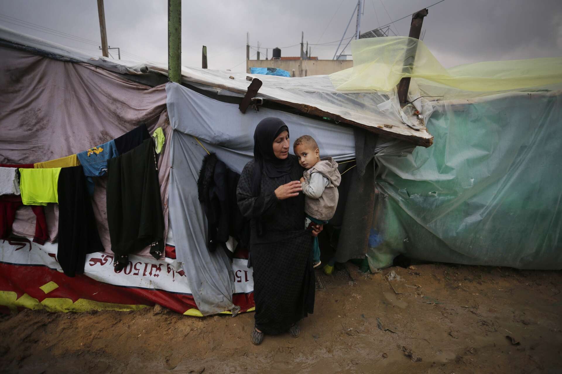 가자 지구의 임시 대피소 밖에서 한 여성이 어린 아이를 안고 있습니다.