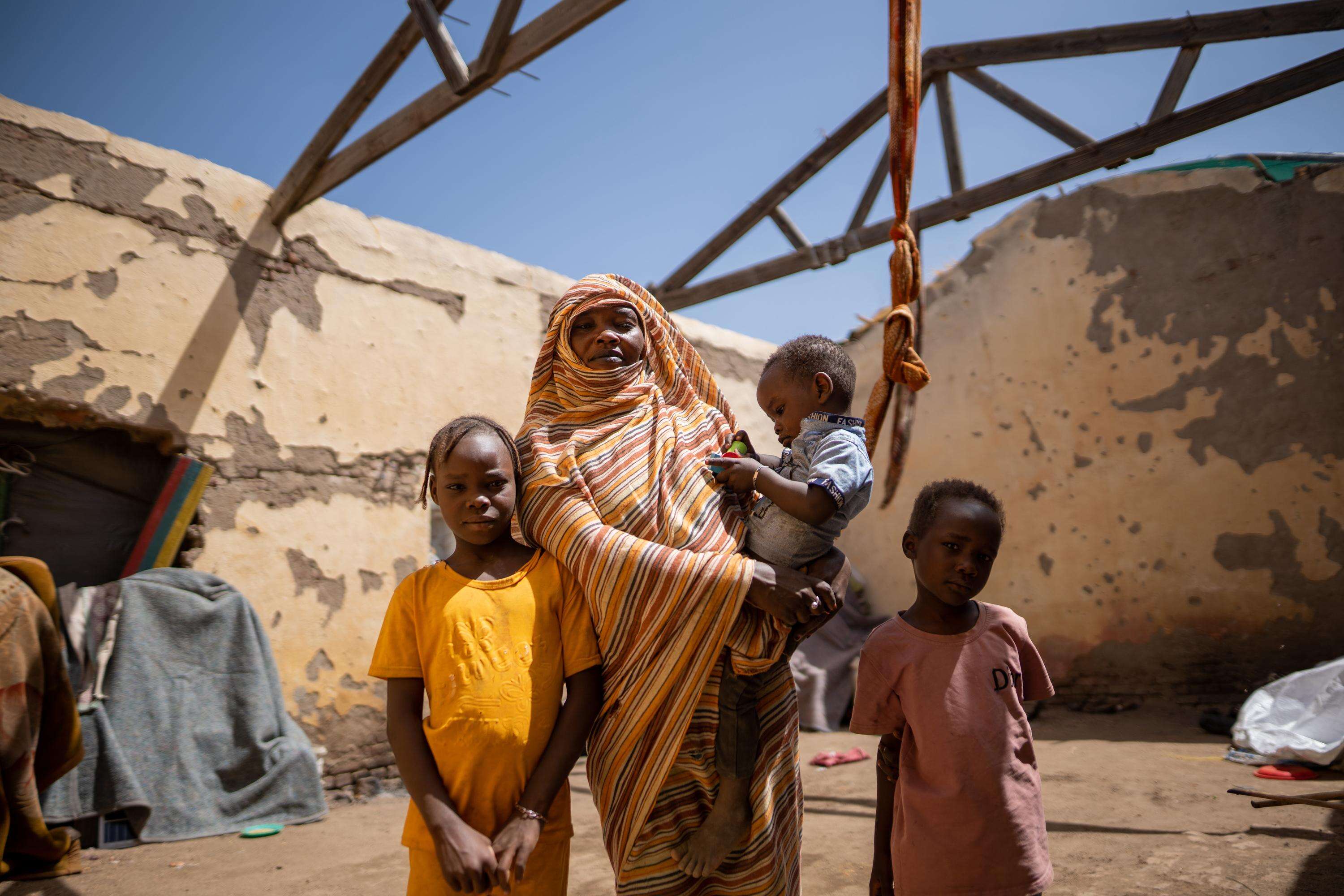 March 26, 2024 - Gedaref, Sudan. Altuma (45), and her children stand inside their roofless shelter.