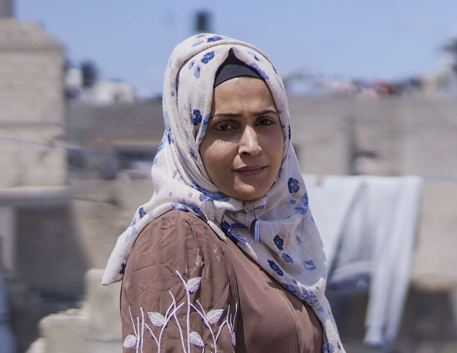 A woman in a white hijab and brown burqa turns and looks into the camera