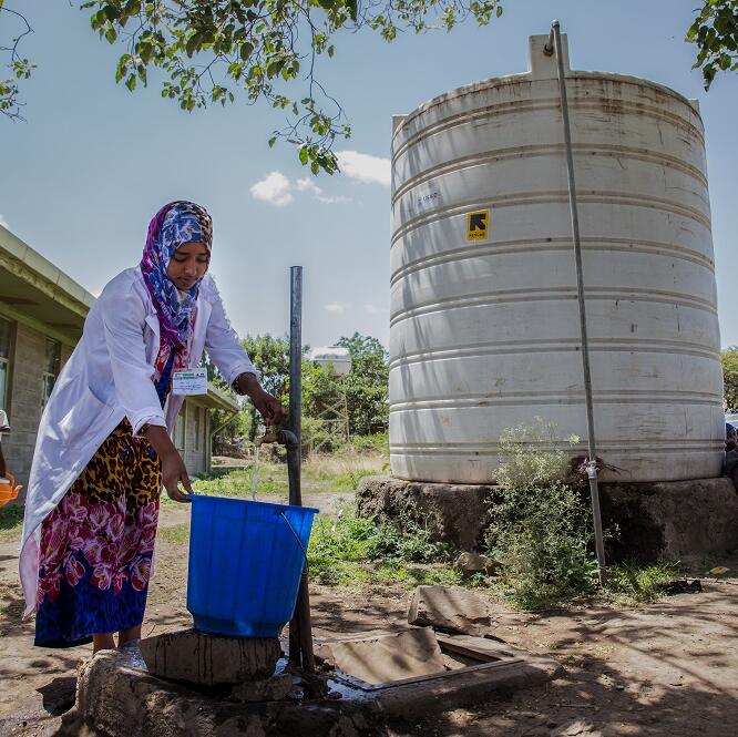 A woman holds out a bucket under a running tap to collect water
