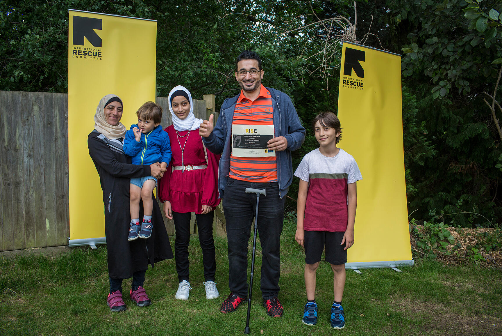 IRC client Khalil holds his RISE certificate and smiles with his wife and children.