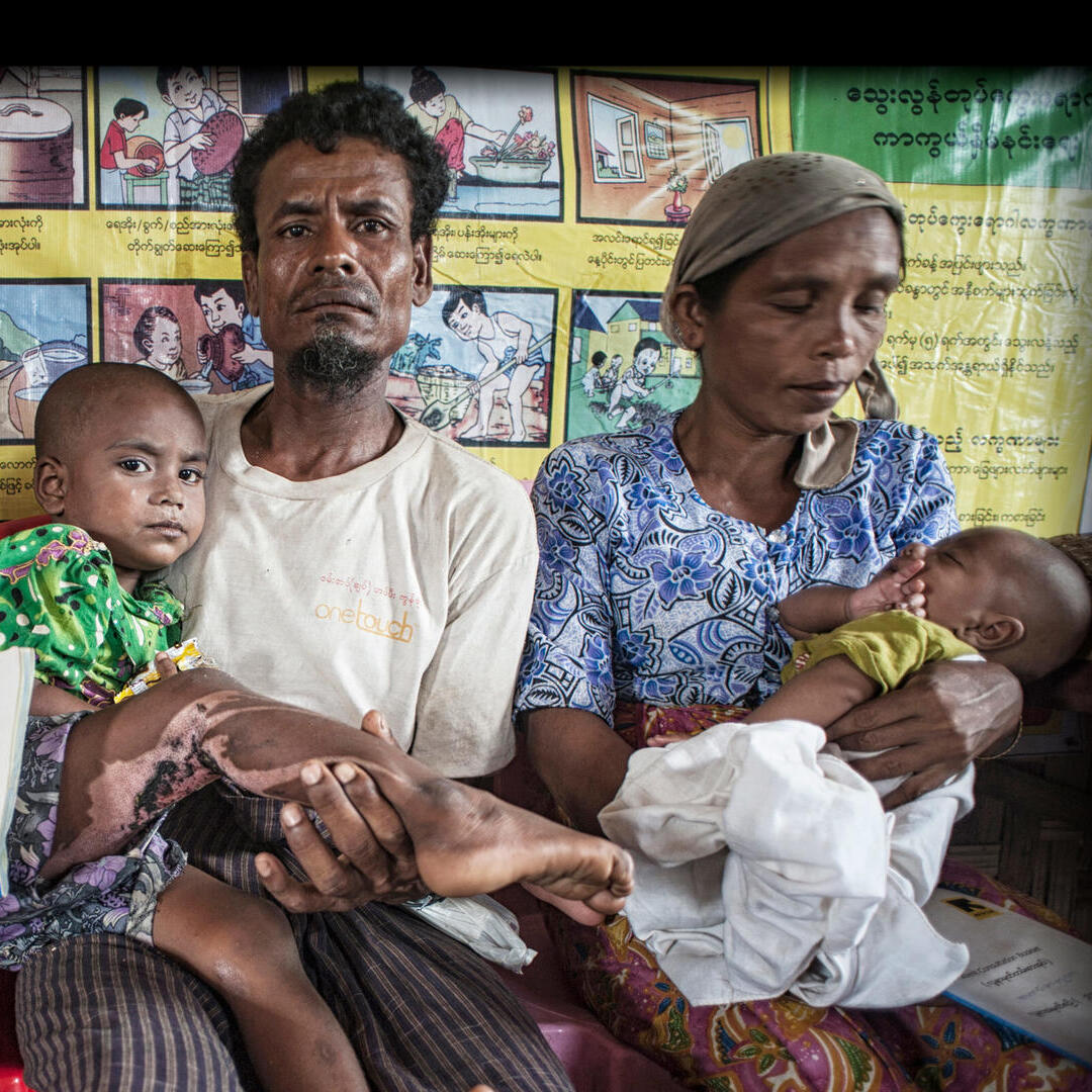 Surrounded by other waiting families, a man holds a young child he has brought to an IRC health center in Myanmar for treatment.