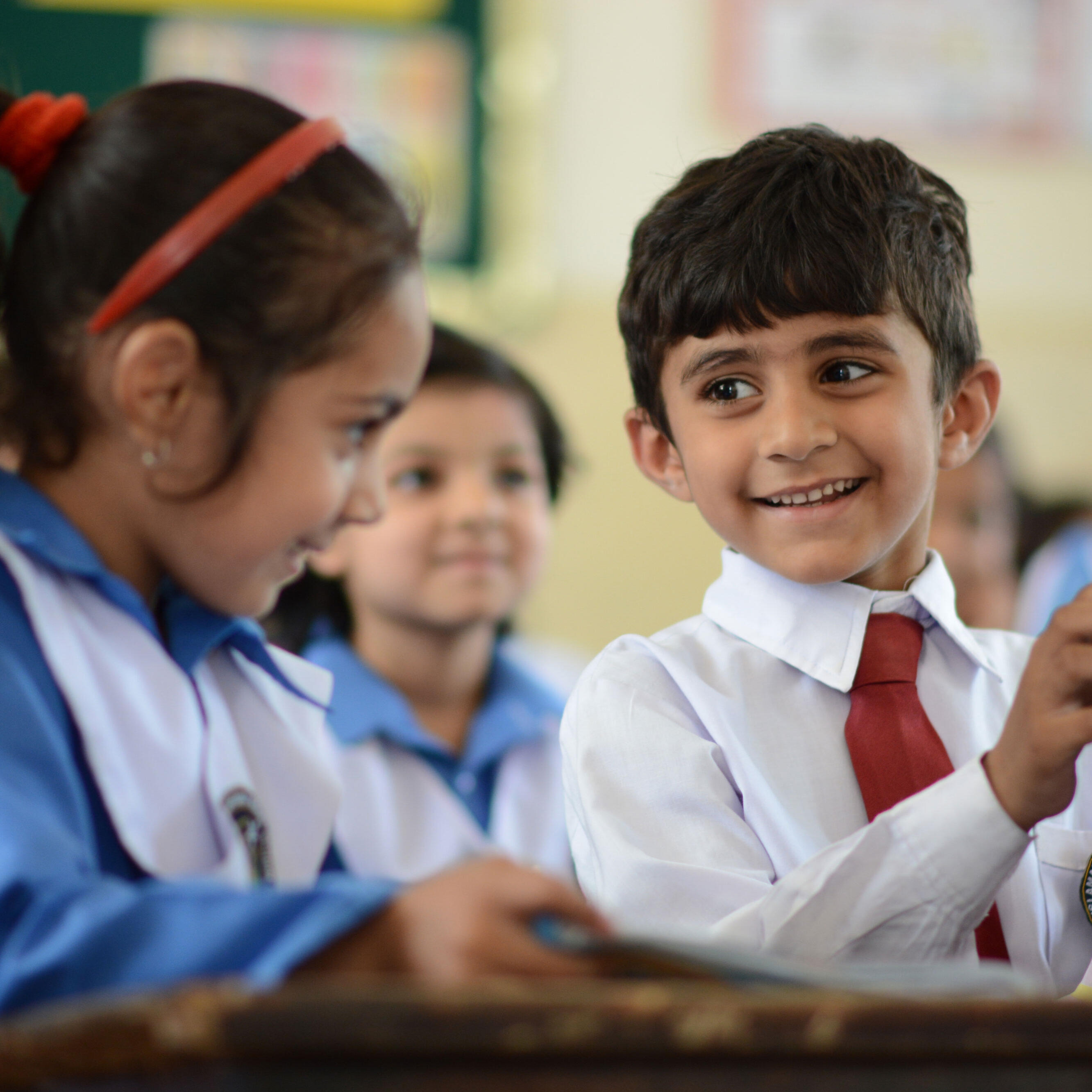 A young student smiles and shows a female classmate a page in his school workbook.