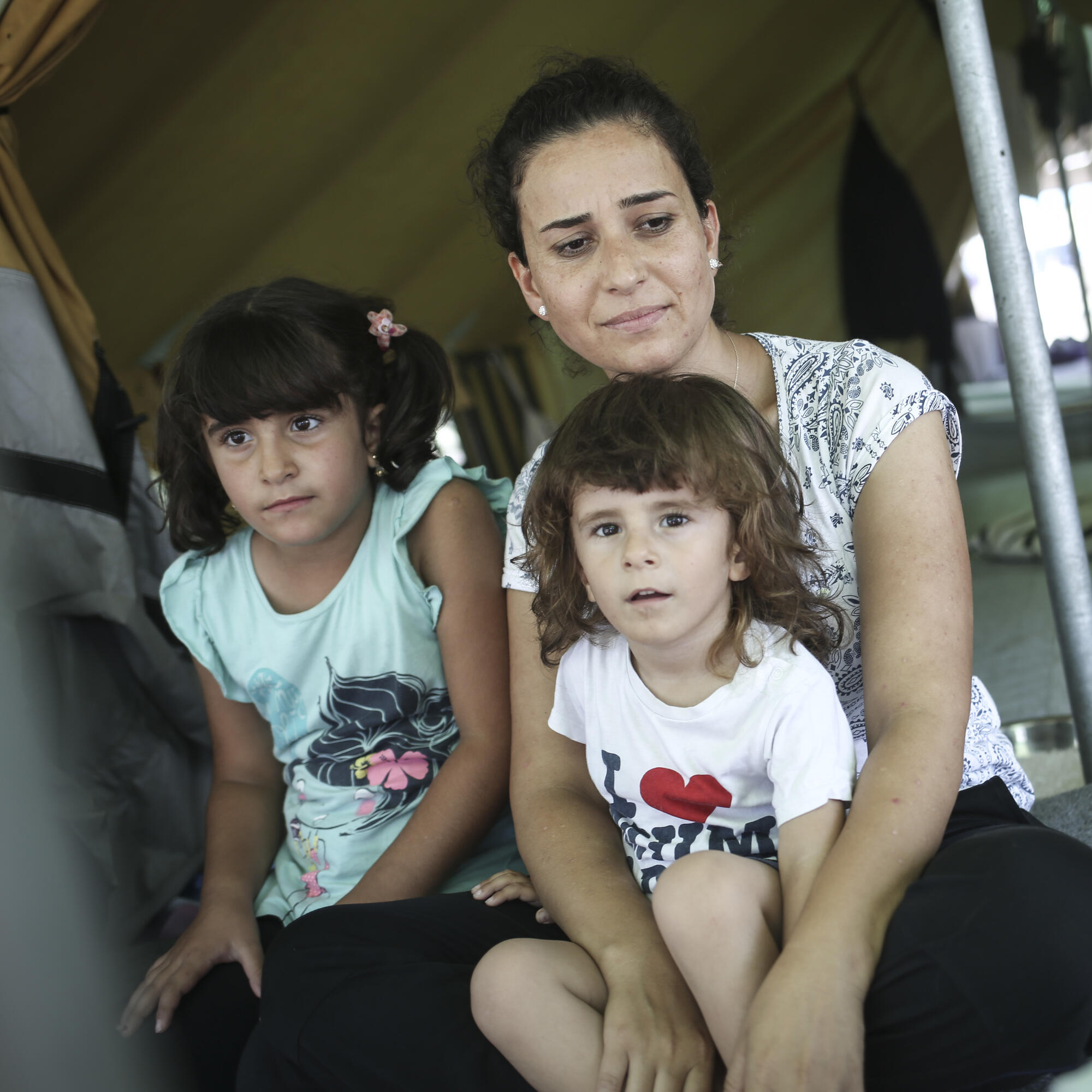 A Syrian refugee woman sits with her son and other family members inside a tent.