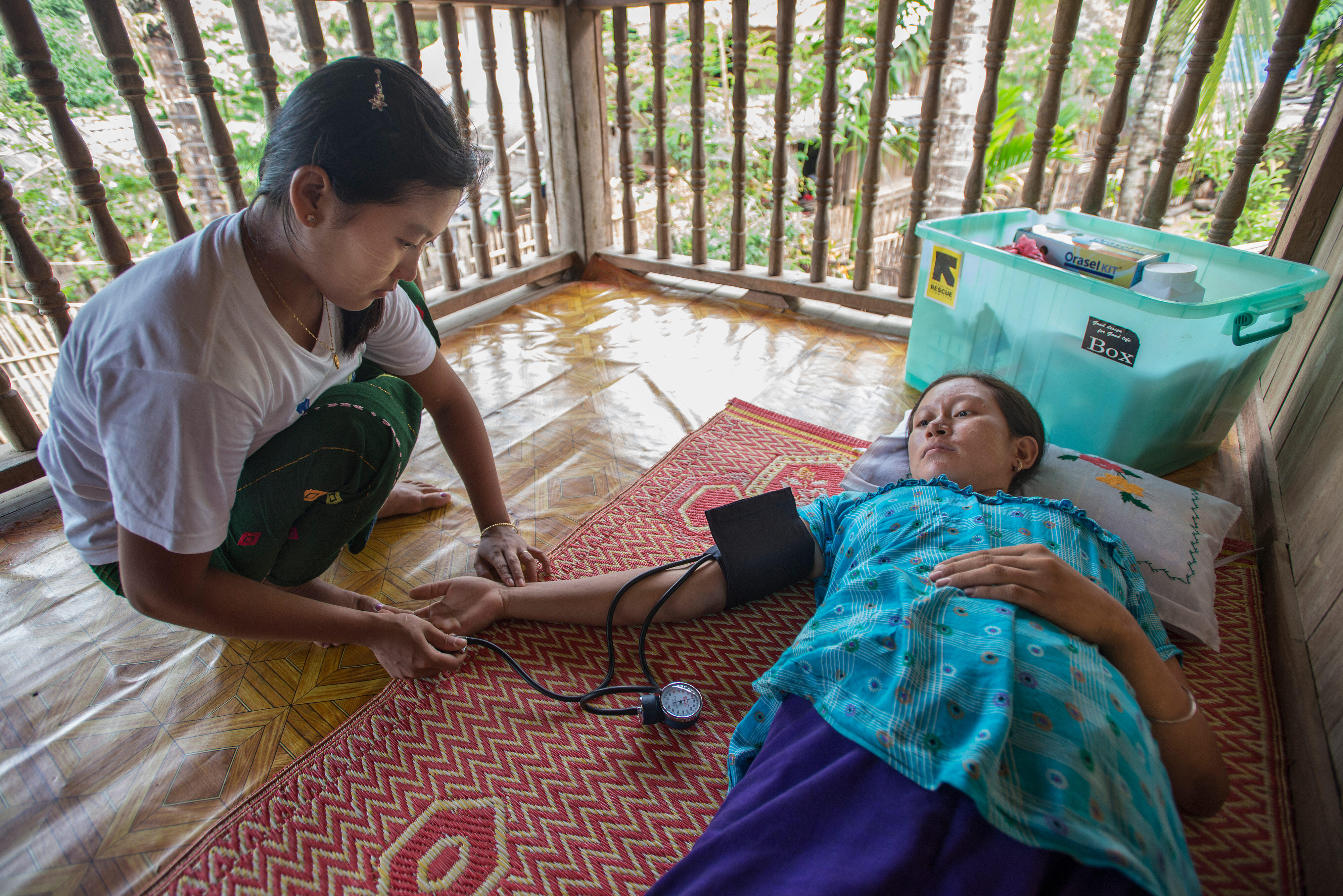 An IRC health worker takes the blood pressure of a female patient lying on a mat on the floor in Thailand.