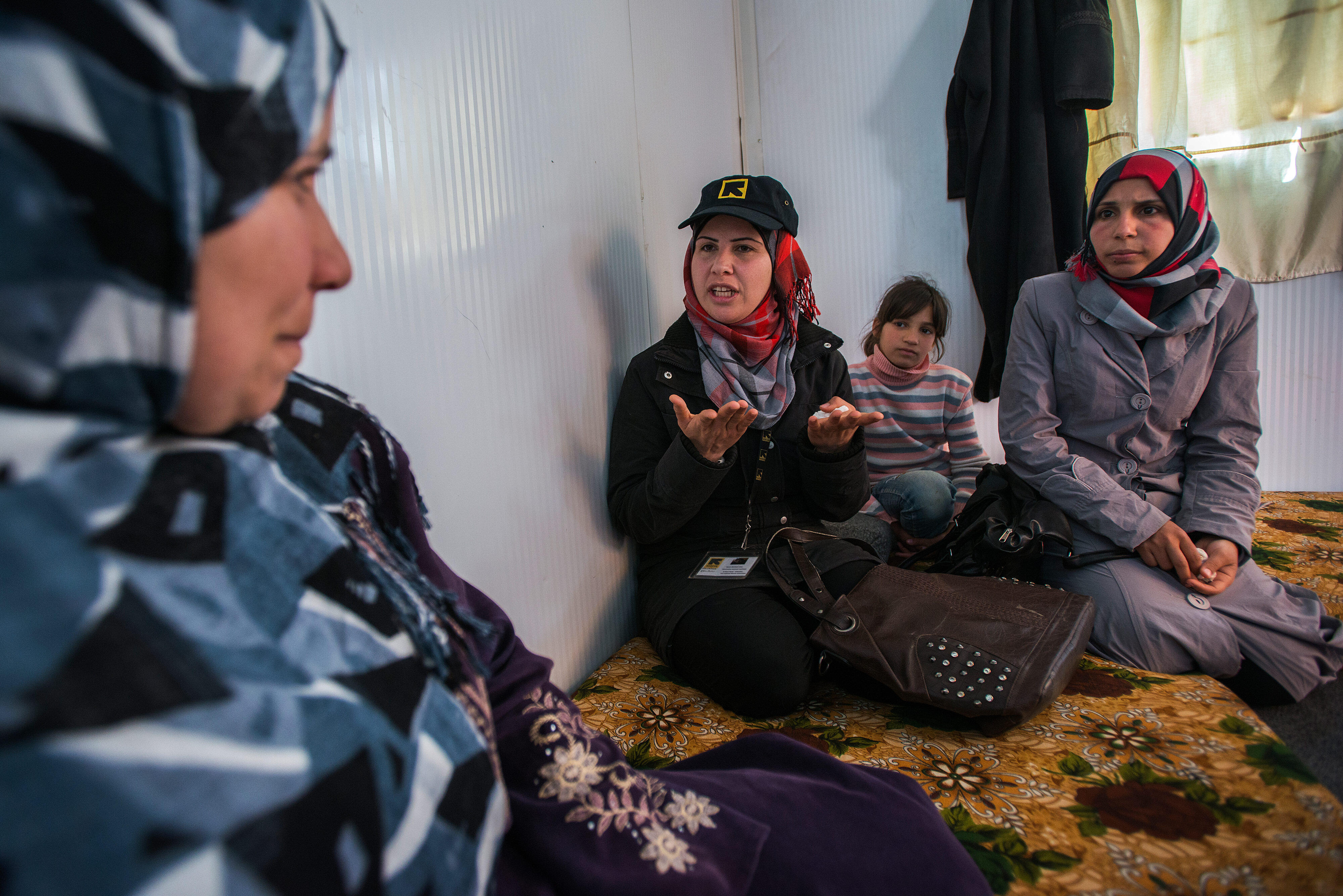 An IRC staff member talks with a Syrian refugee family seated on cushions in their shelter in Zaatari refugee camp in Jordan.