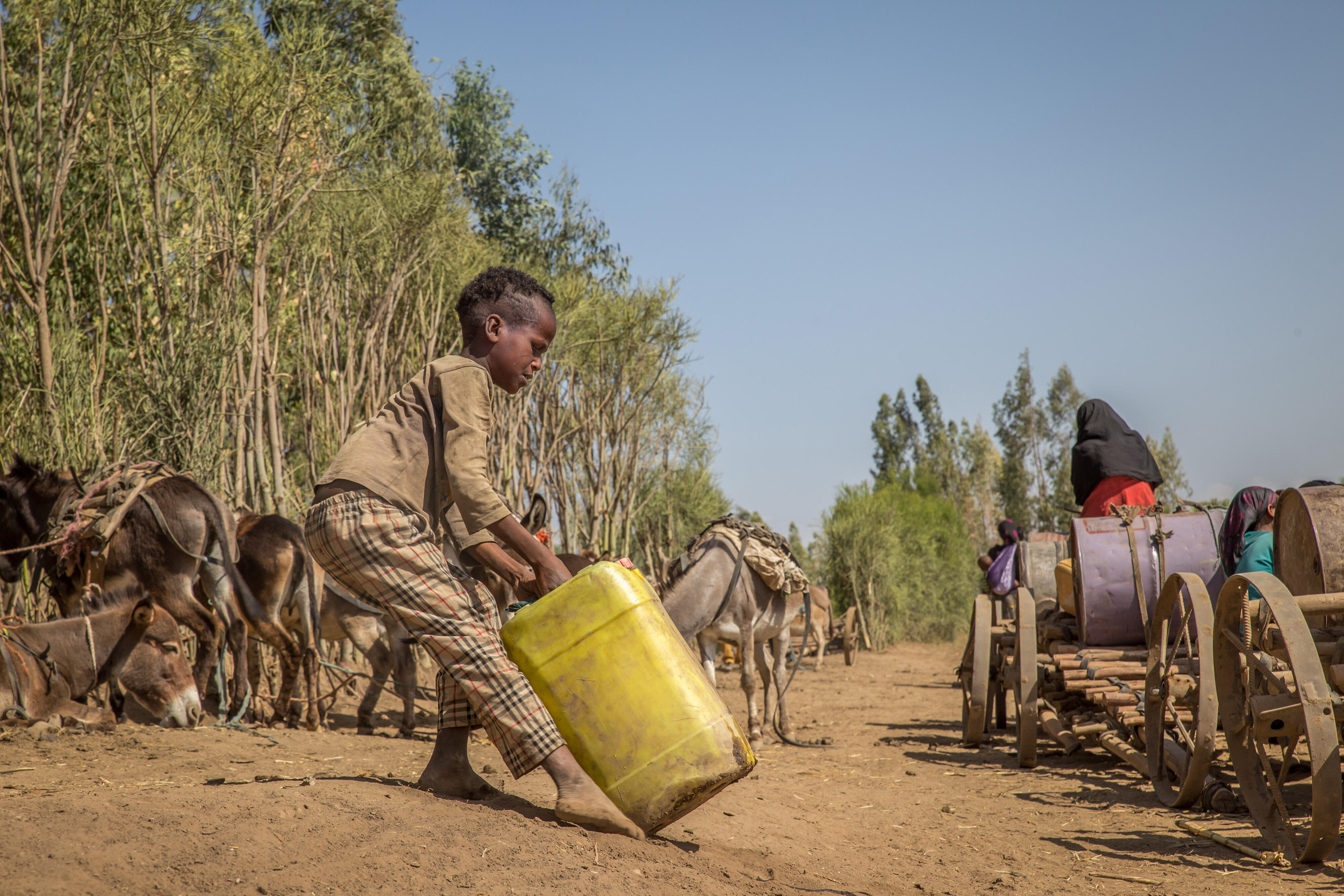 Small boy carries a yellow water container