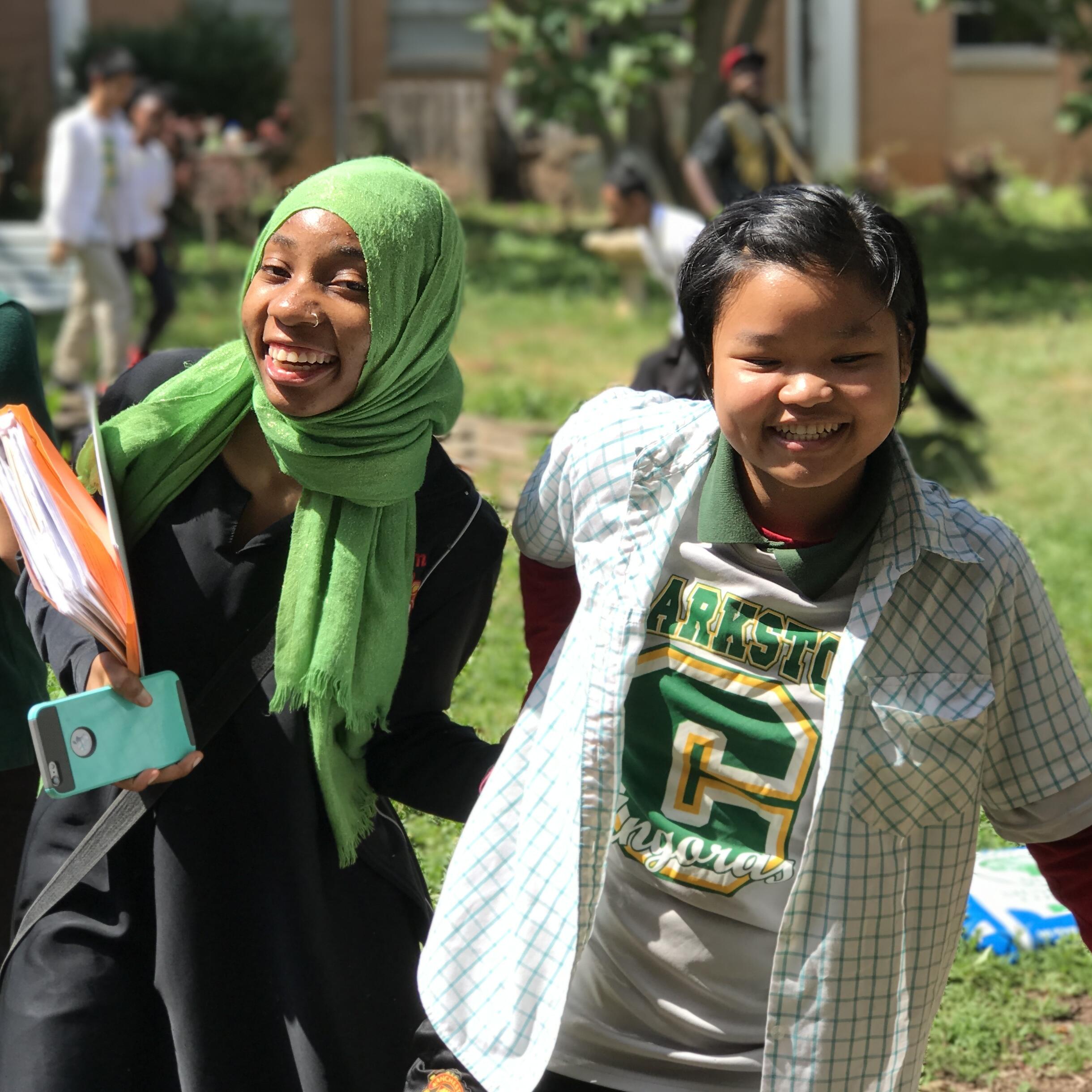 Two students from Burundi and Myanmar hold hands while walking on the lawn outside their school.