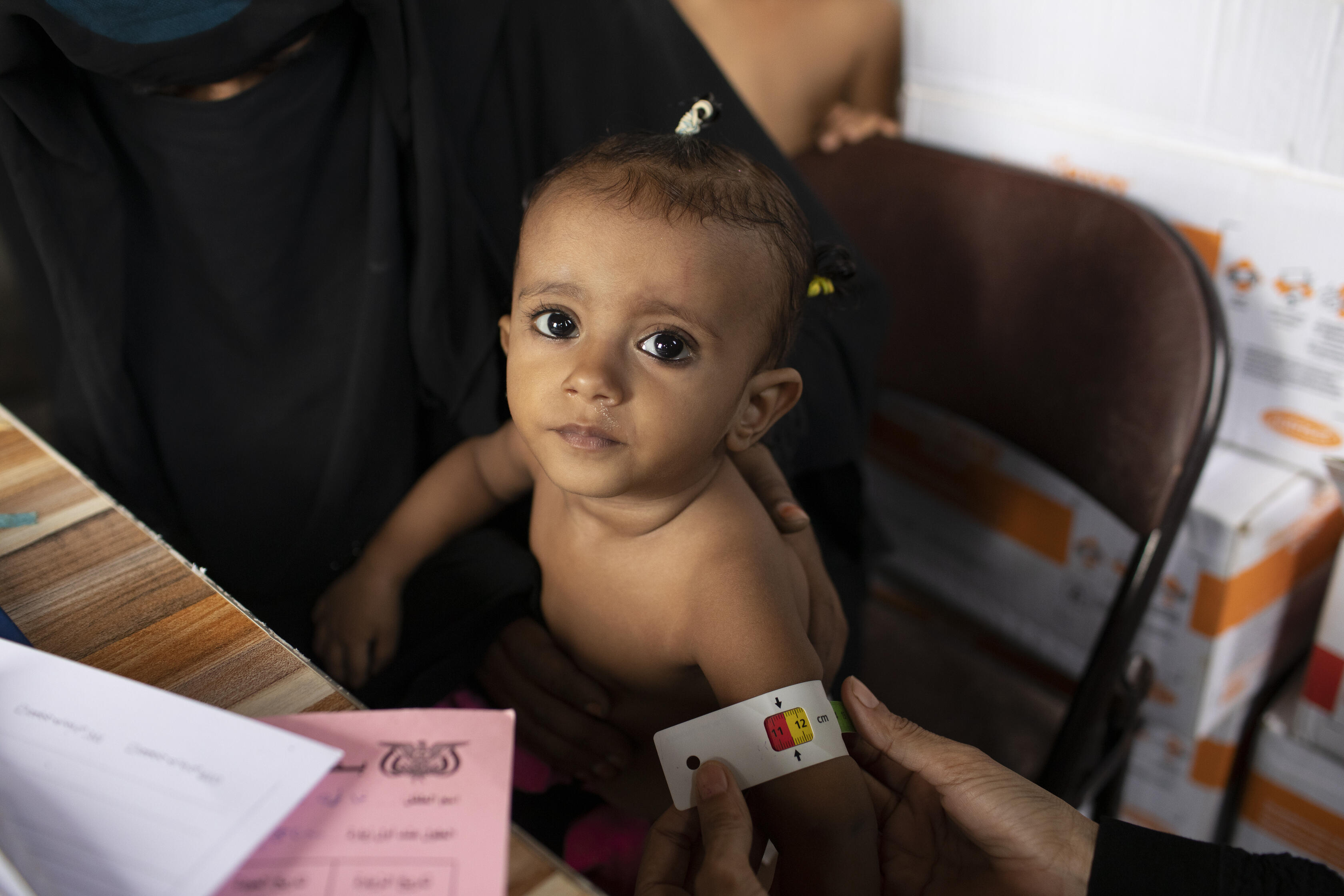 A small child being examined at an IRC clinic in Yemen has her upper arm measured with a MUAC tape, which shows she may be acutely malnourished.