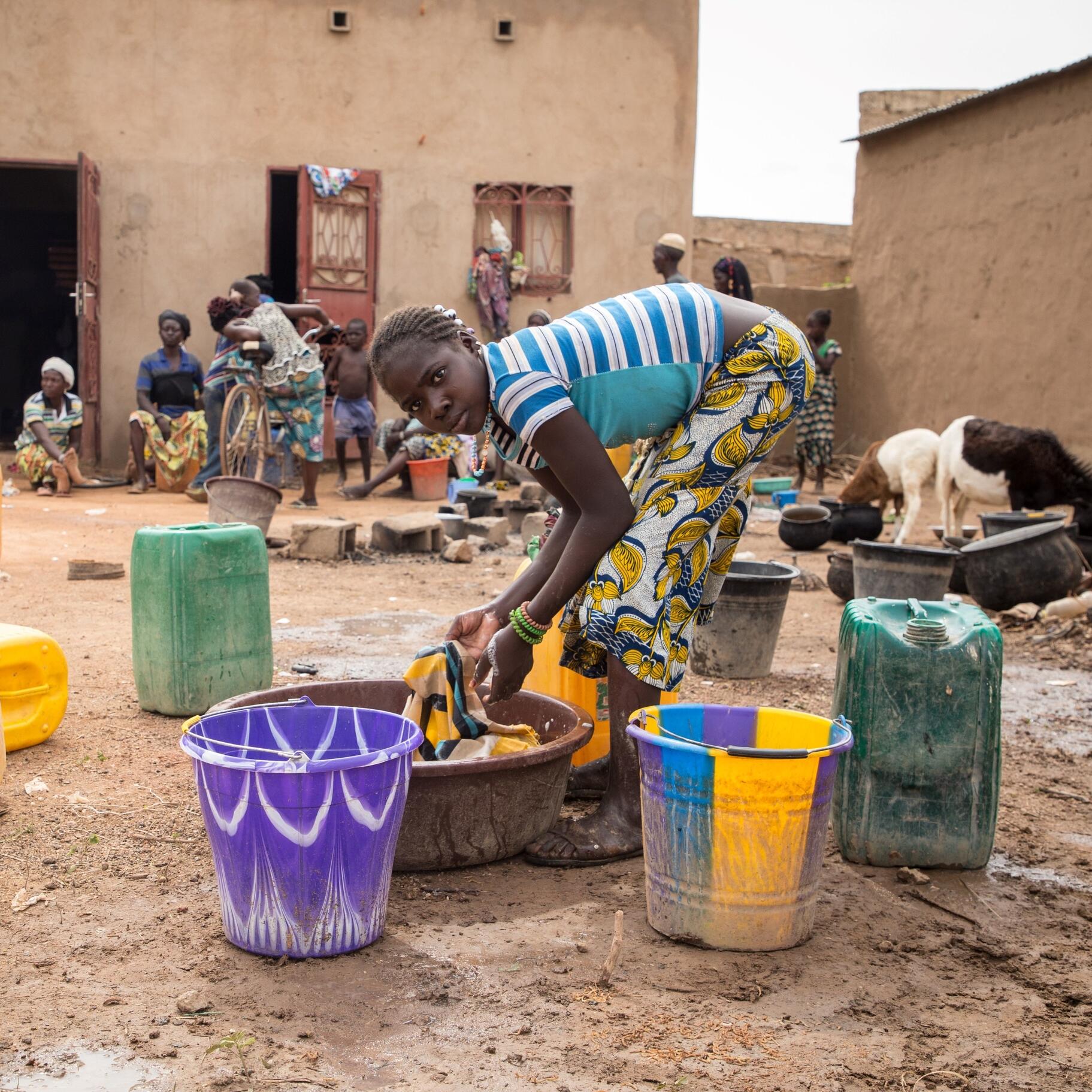 A girl washes clothes as families stand outside a school used as a shelter for Internally Displaced People (IDP) from northern Burkina Faso on June 13, 2019 in Ouagadougou.